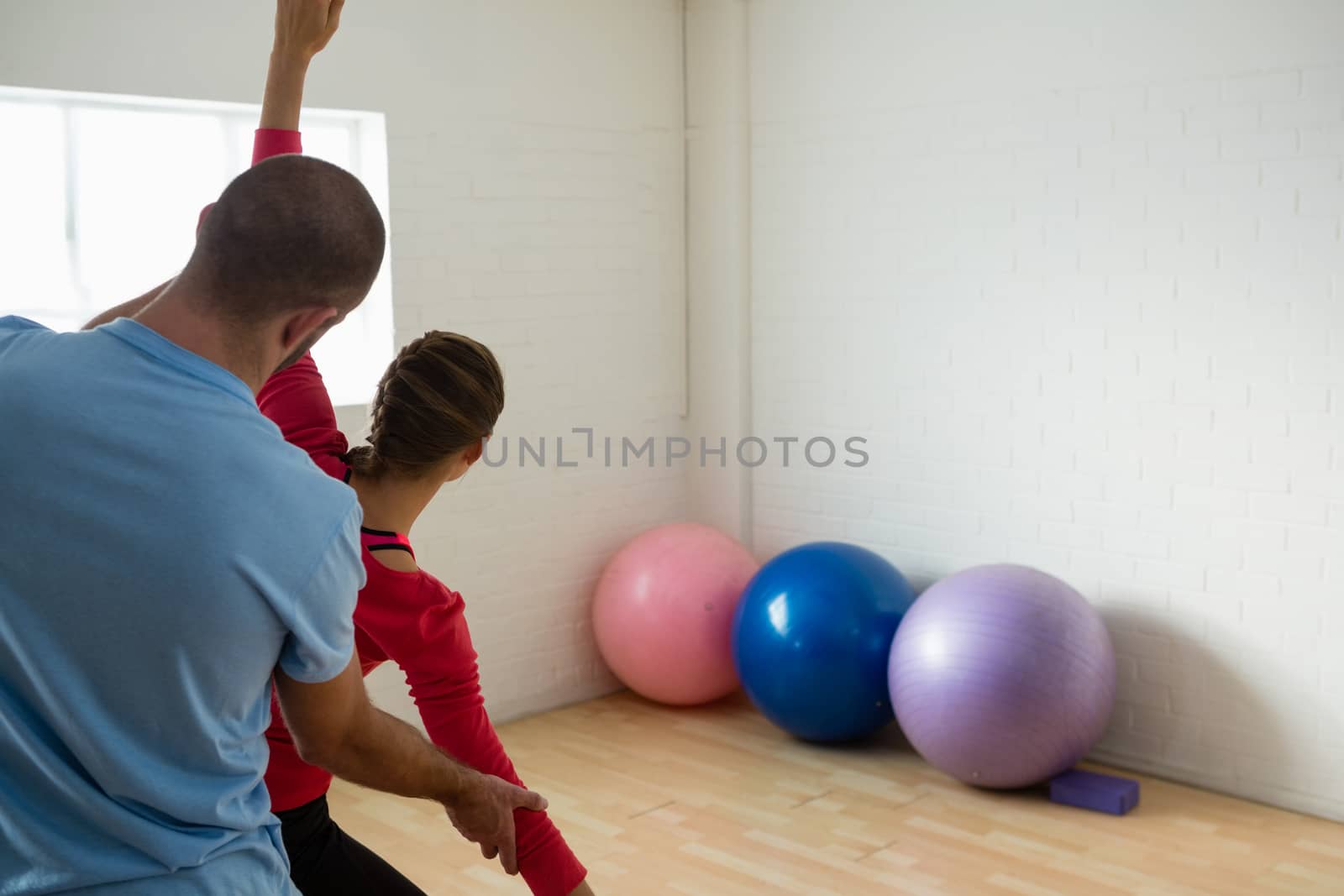 Rear view of instructor assisting student in exercising at yoga studio by Wavebreakmedia