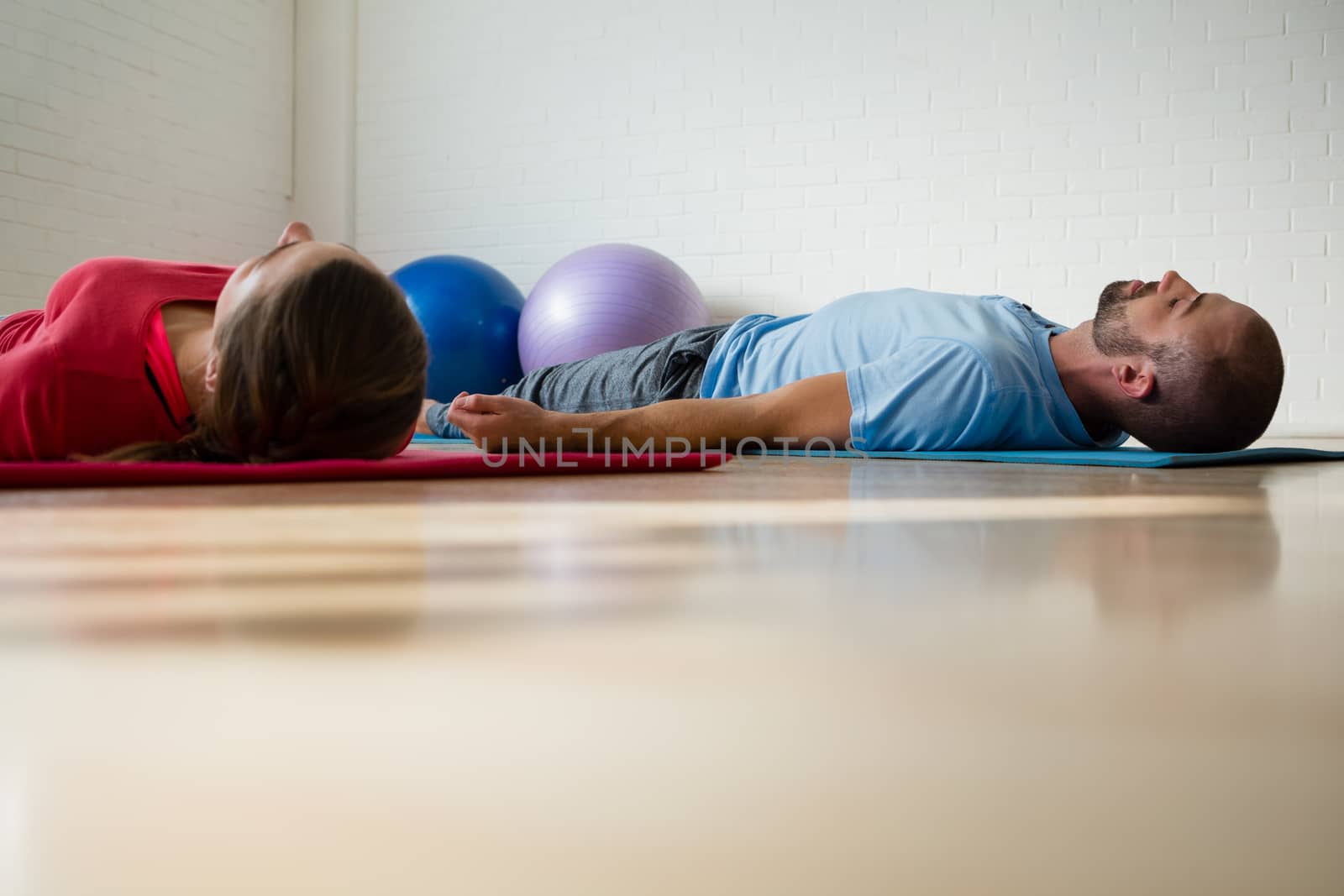 Instructor and student exercising while lying on mat in yoga studio