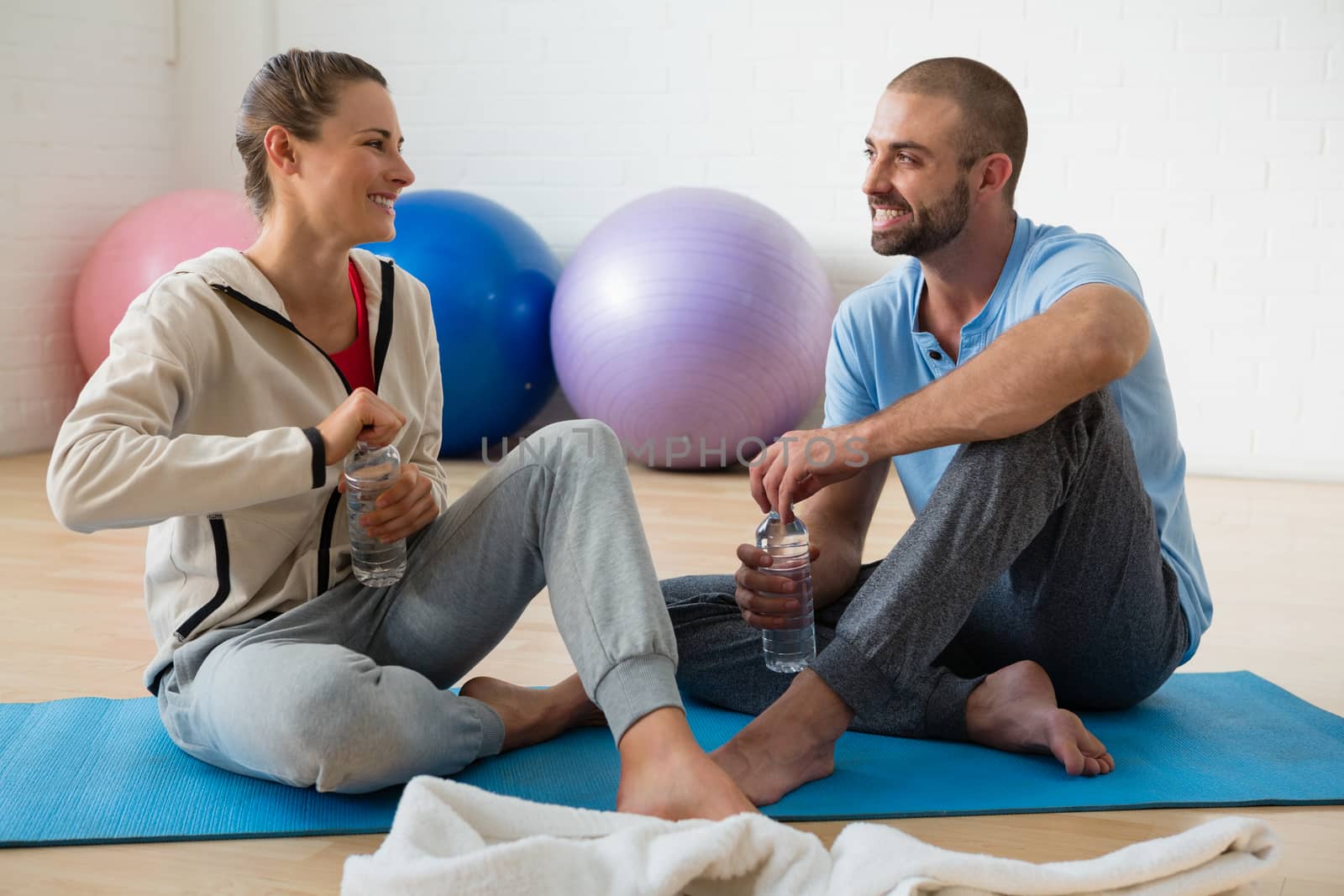 Instructor and student talking while having water in yoga studio by Wavebreakmedia