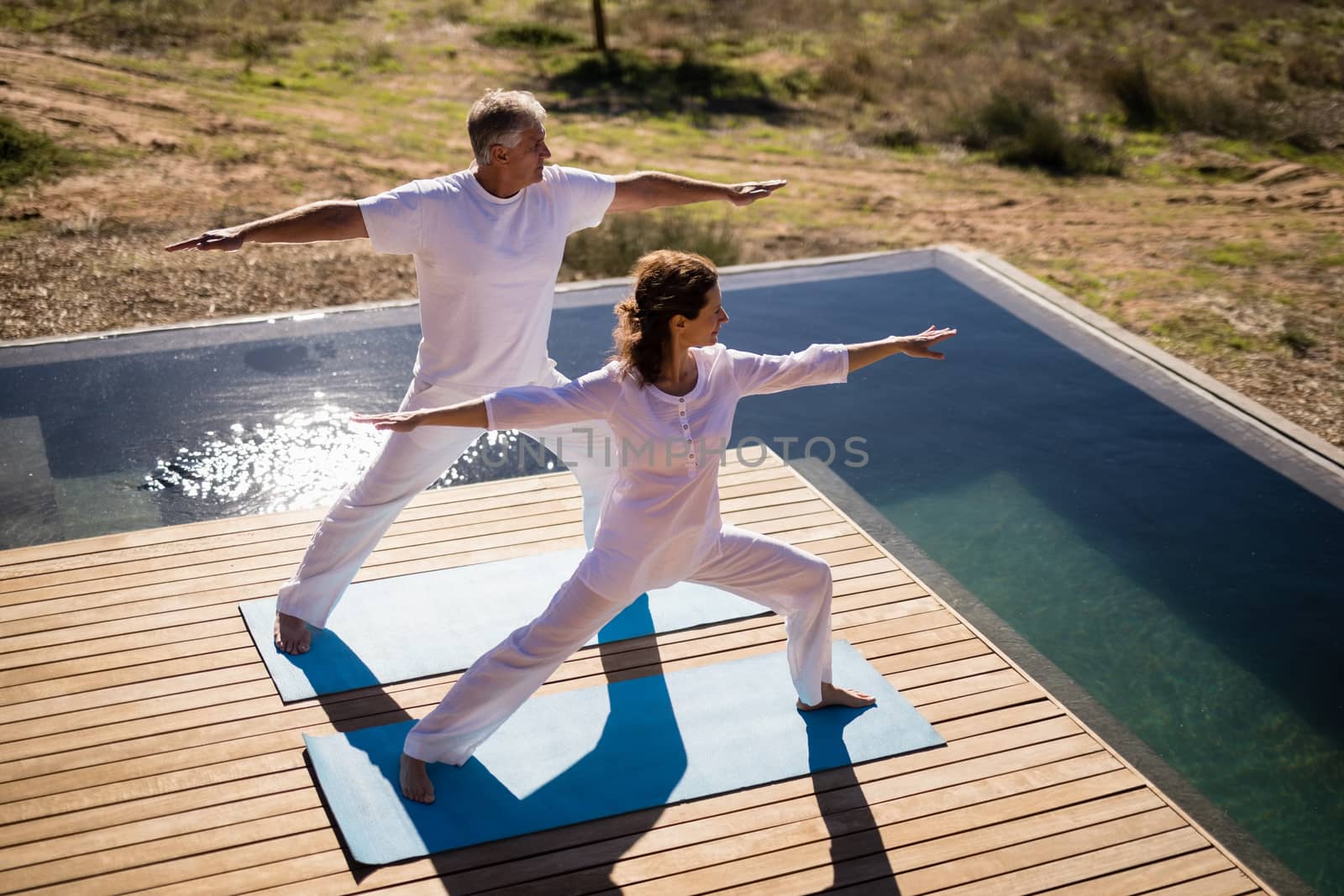 Couple practicing yoga on at poolside on a sunny day