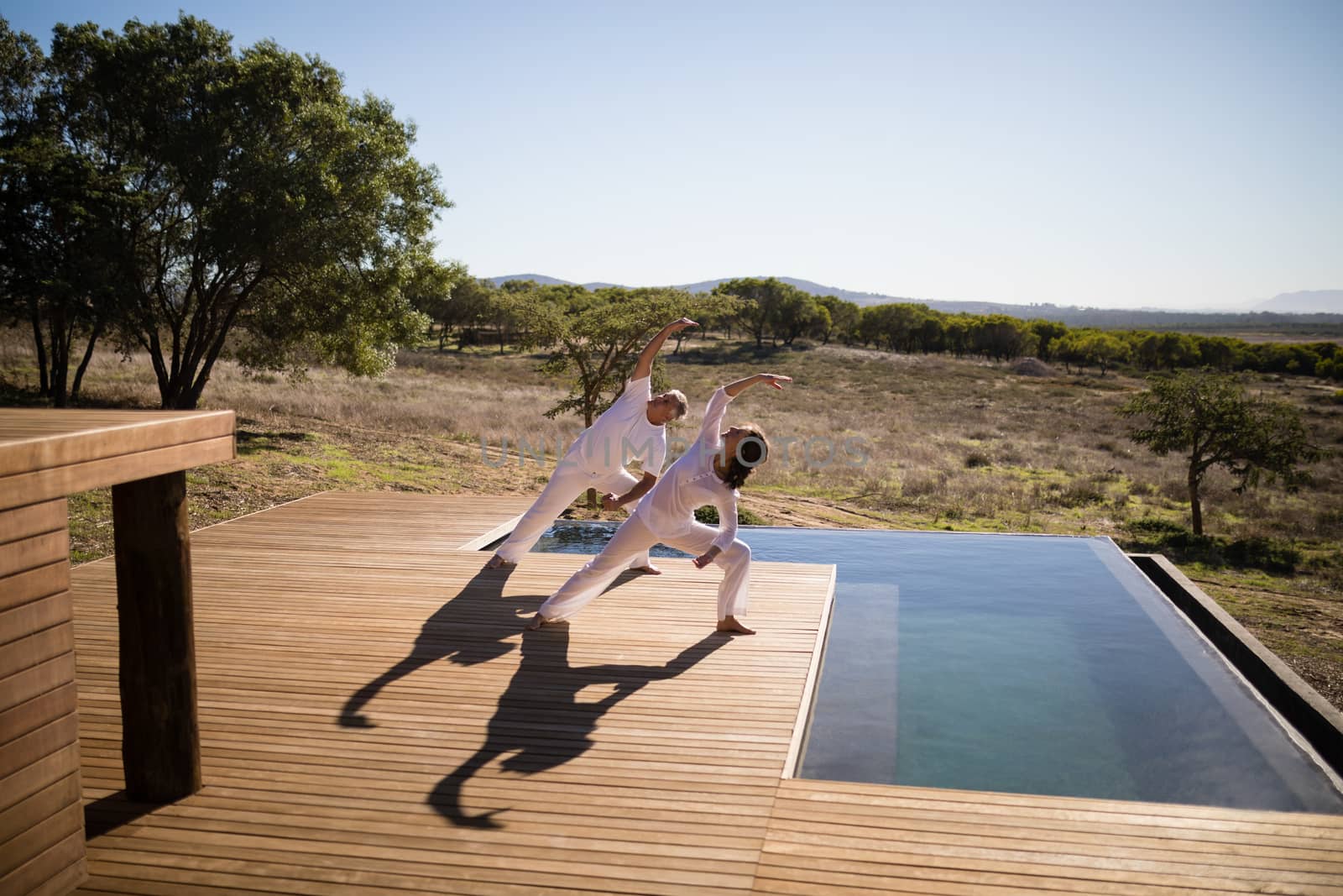 Couple practicing yoga on wooden plank by Wavebreakmedia