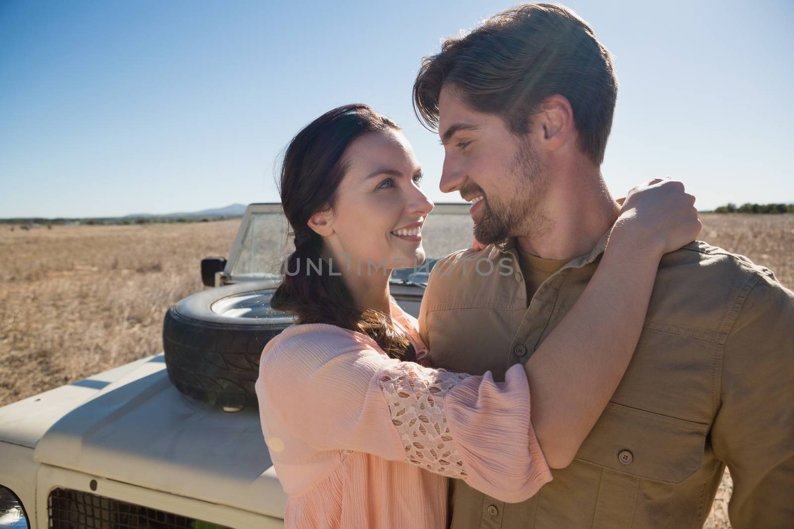 Romantic couple looking each other by off road vehicle on landscape