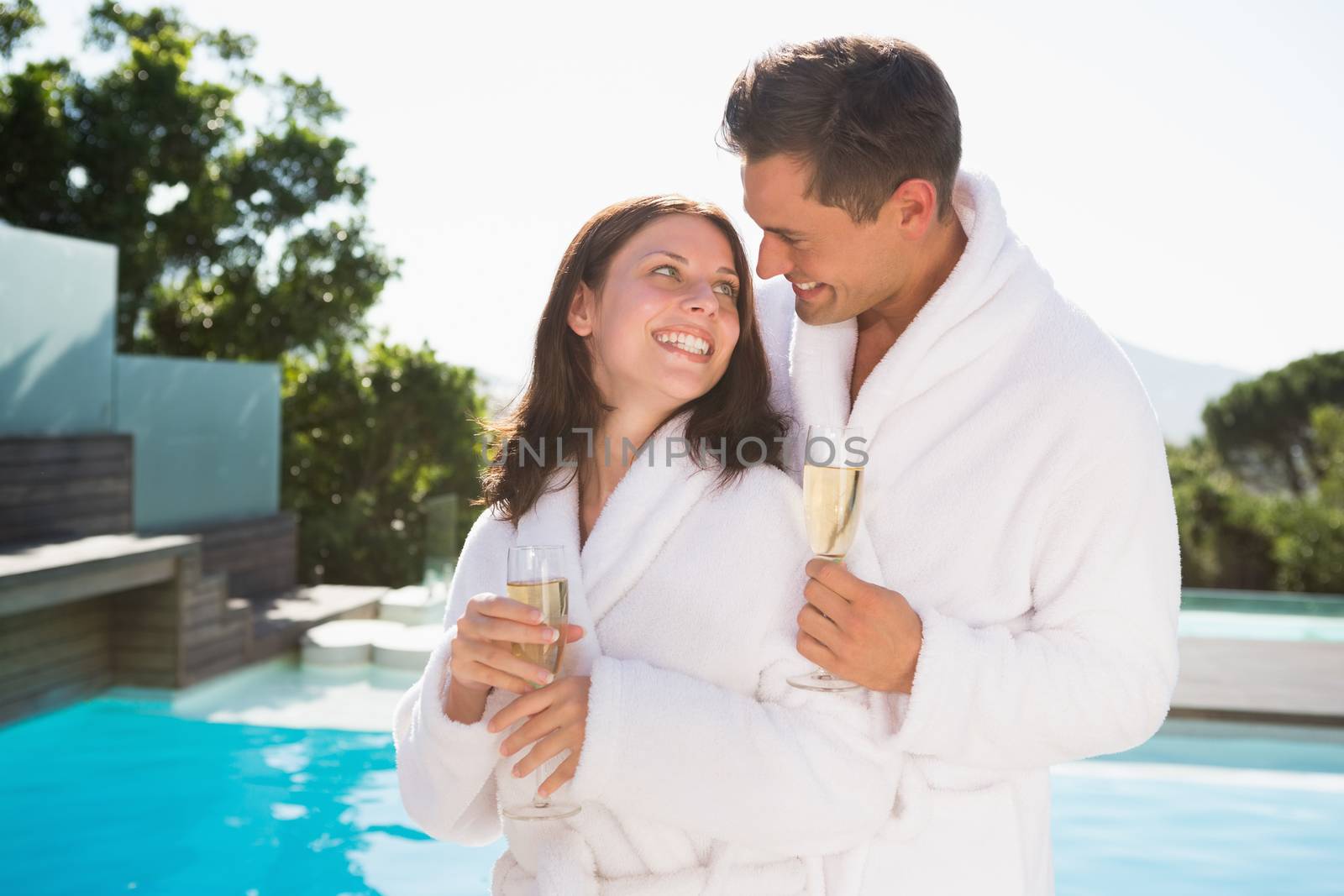 Happy romantic young couple with champagne flutes by swimming pool