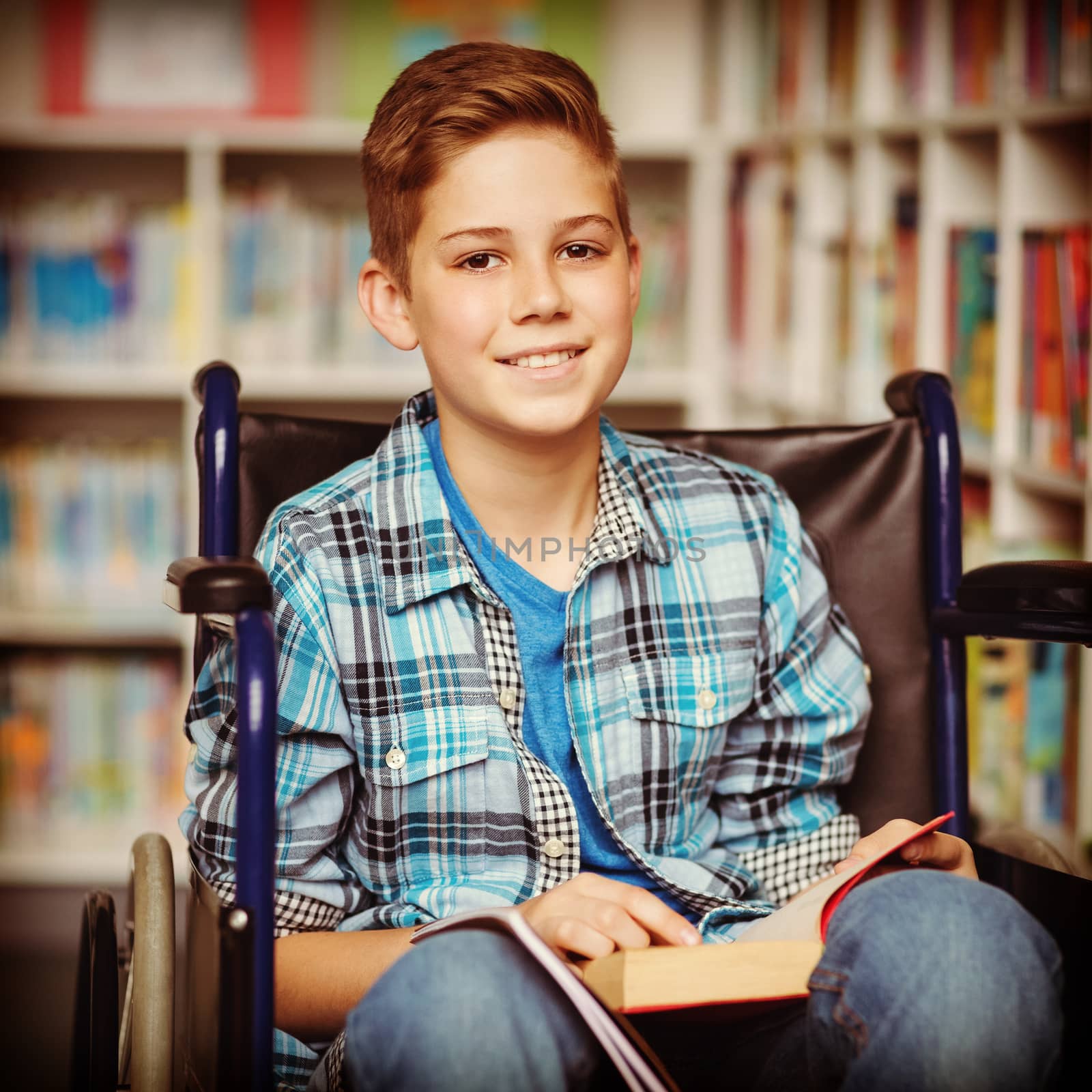 Portrait of disabled schoolboy holding book in library at school