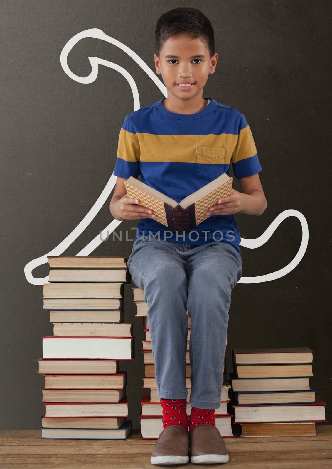 Digital composite of Student boy on a table reading against grey blackboard with school and education graphic