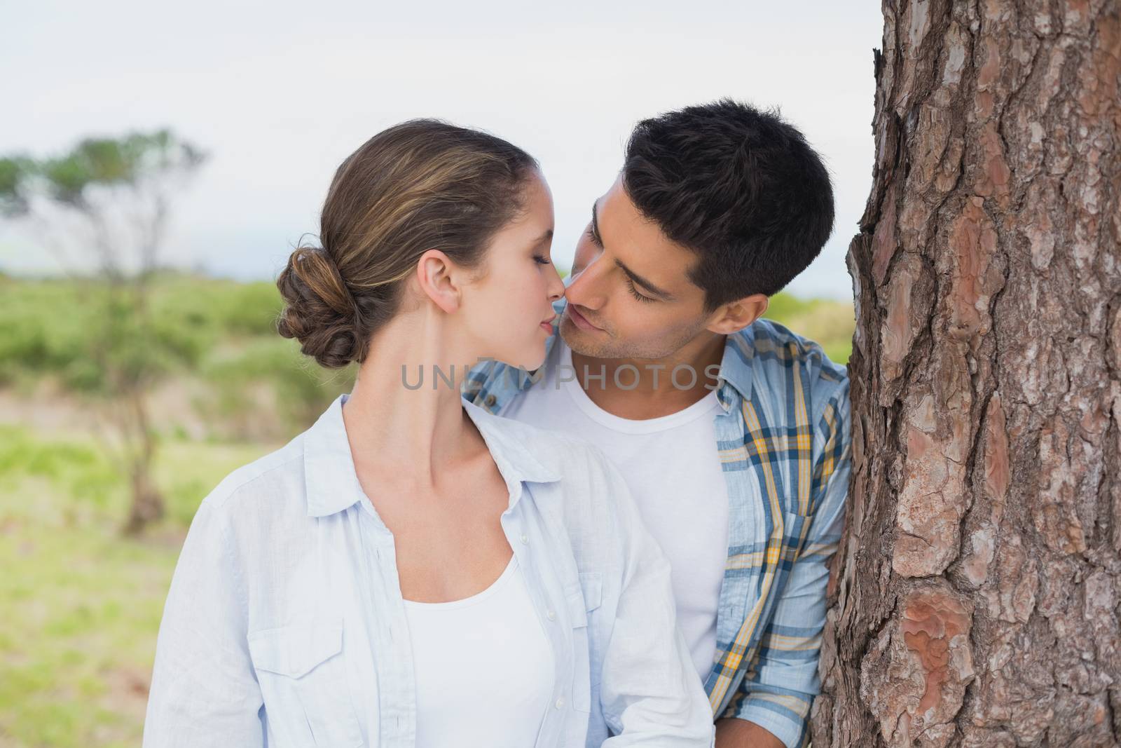 Close up of a romantic young couple about to kiss by tree trunk