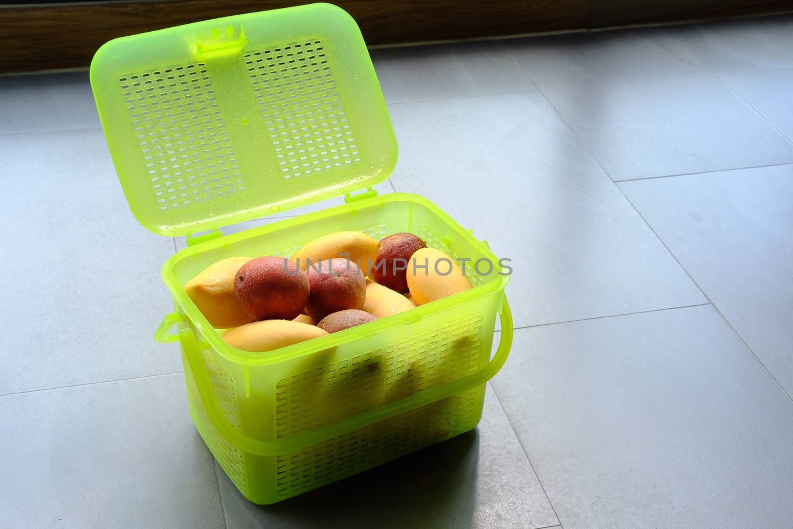 Light-green plastic basket or container with fresh exotic fruits yellow mango and passion. Top view close up.