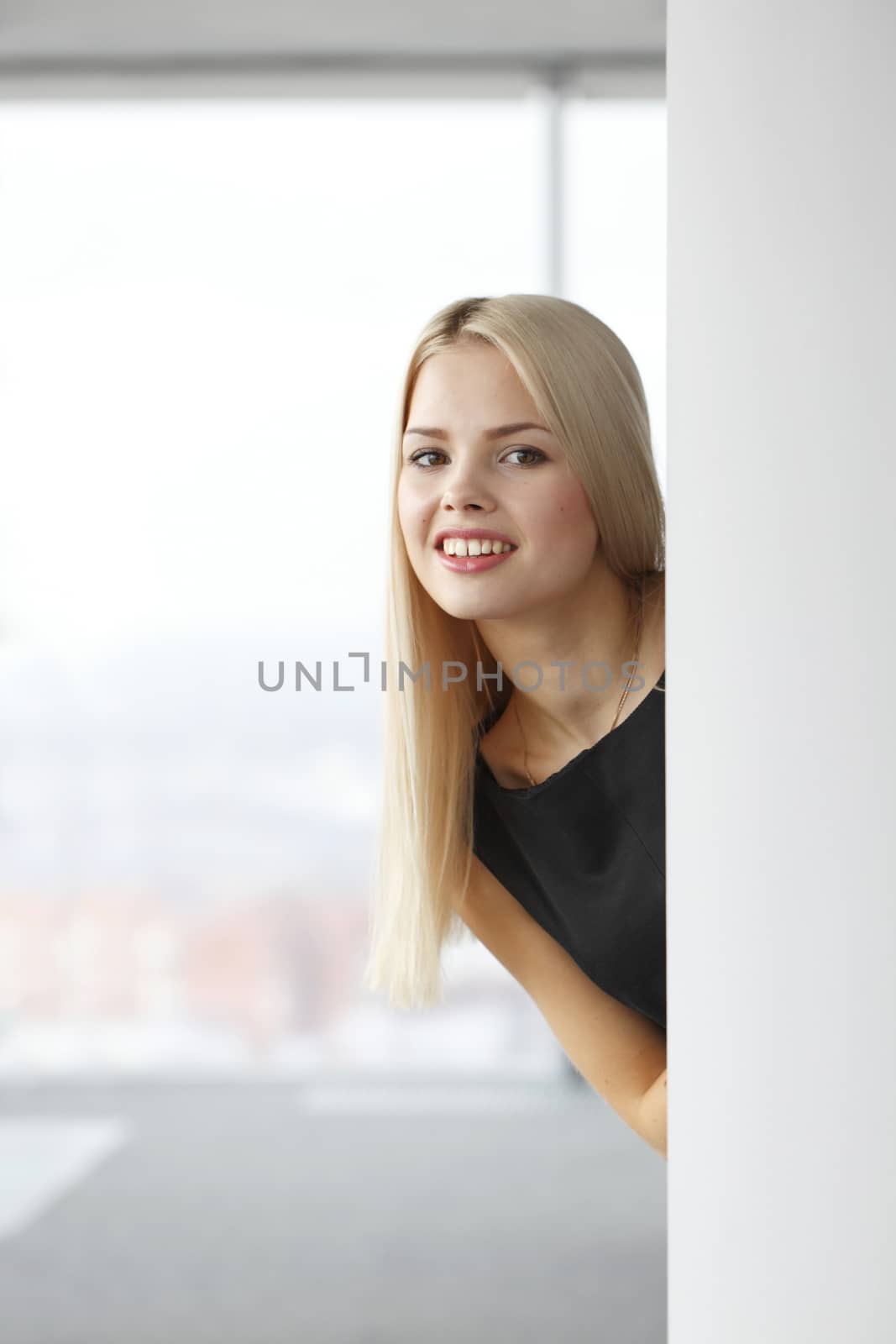 A portrait of a young business woman in an office looking out from corner