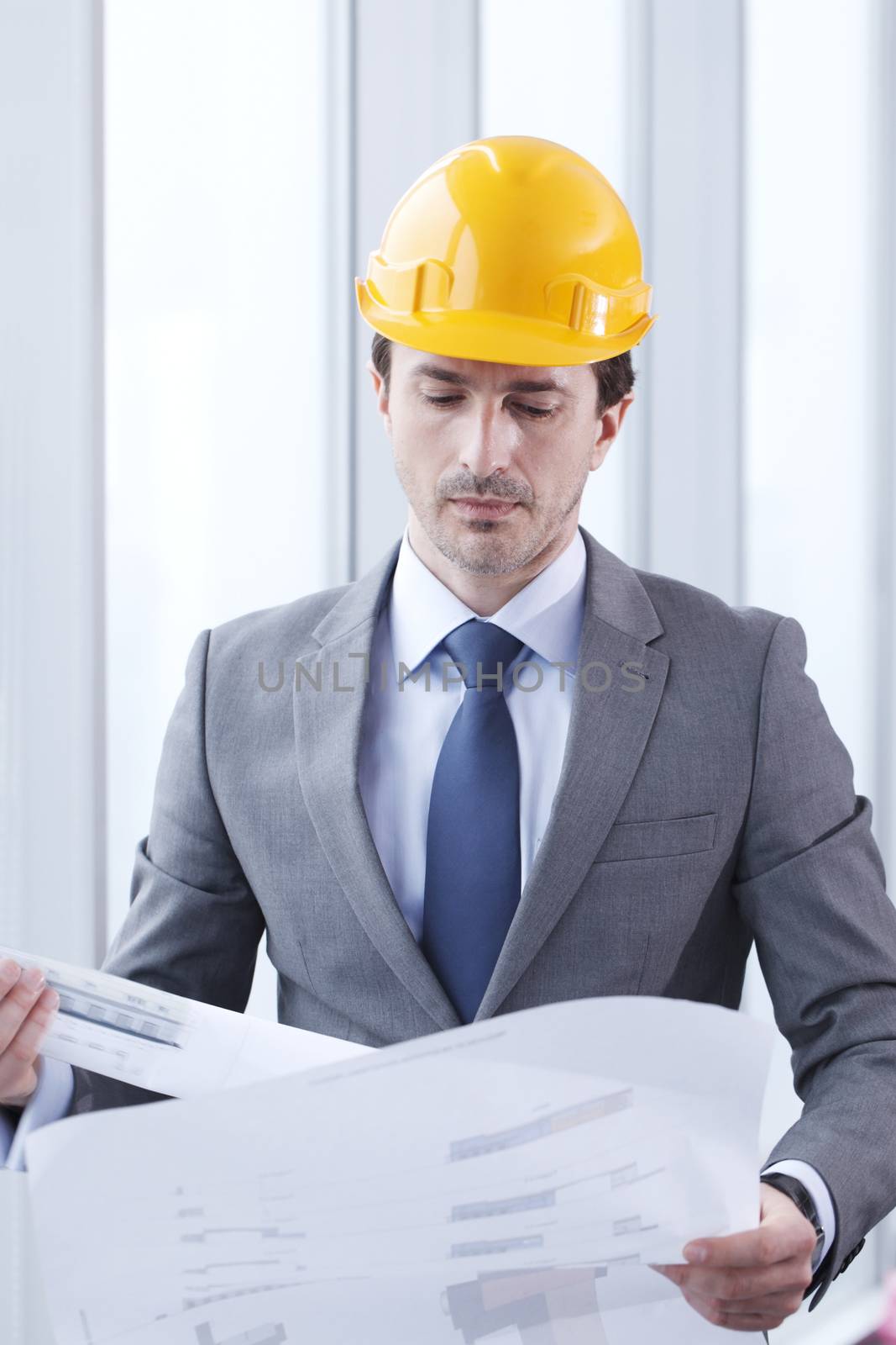 Male business man architect construction engineer in yellow hardhat reading blueprint in office