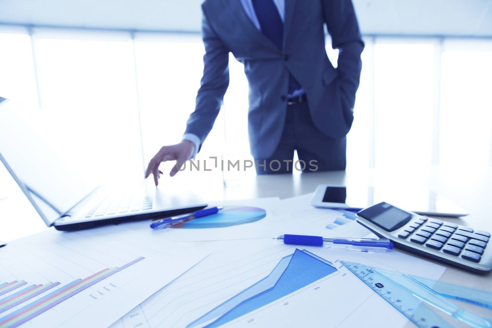 Business documents on office table with laptop and and calculator business diagram and man working in the background