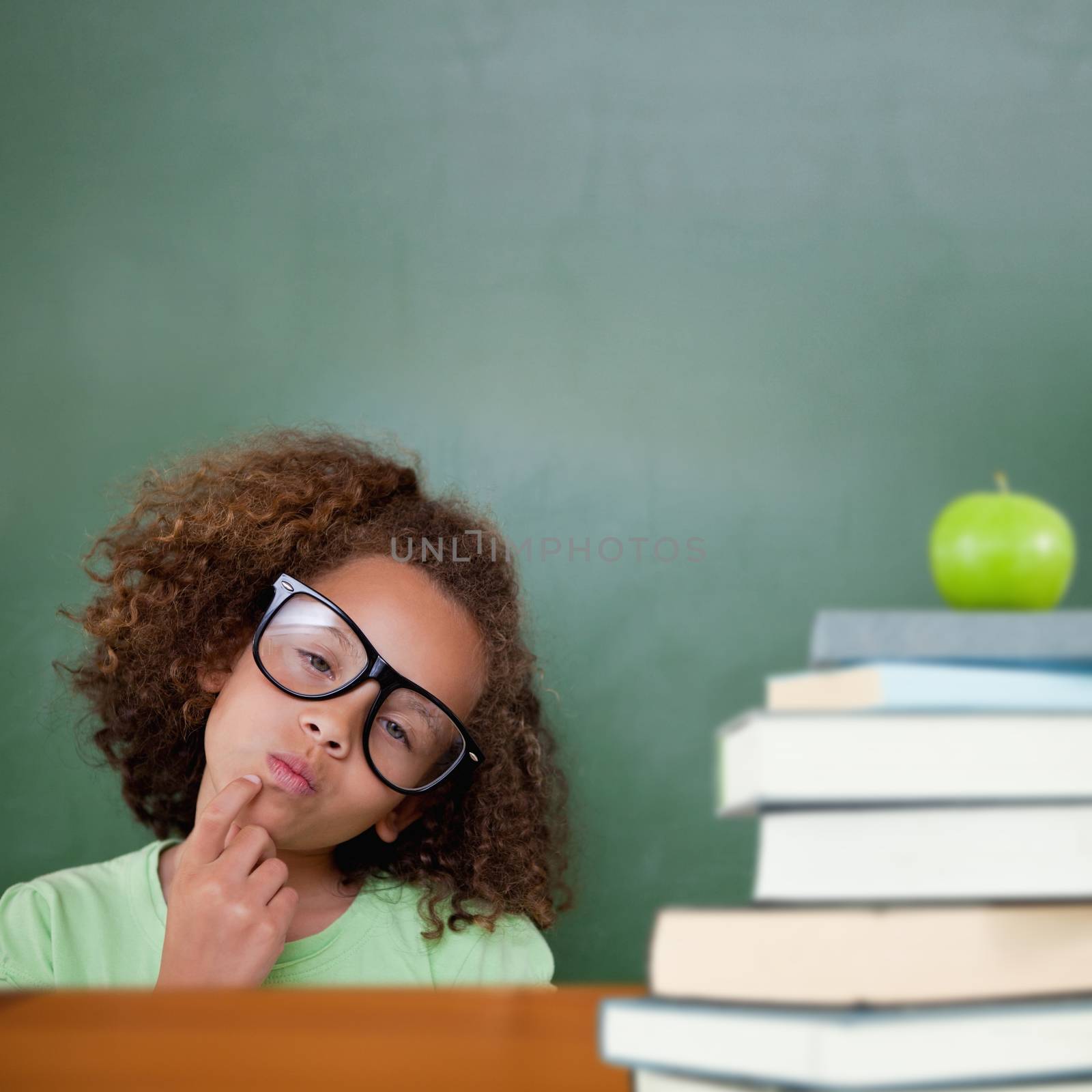 Cute pupil thinking against green apple on pile of books