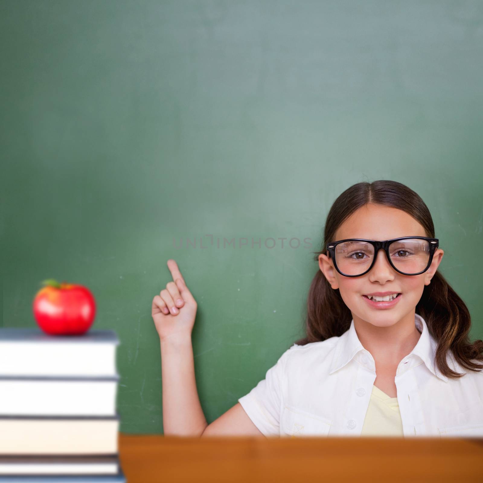 Cute pupil pointing against red apple on pile of books