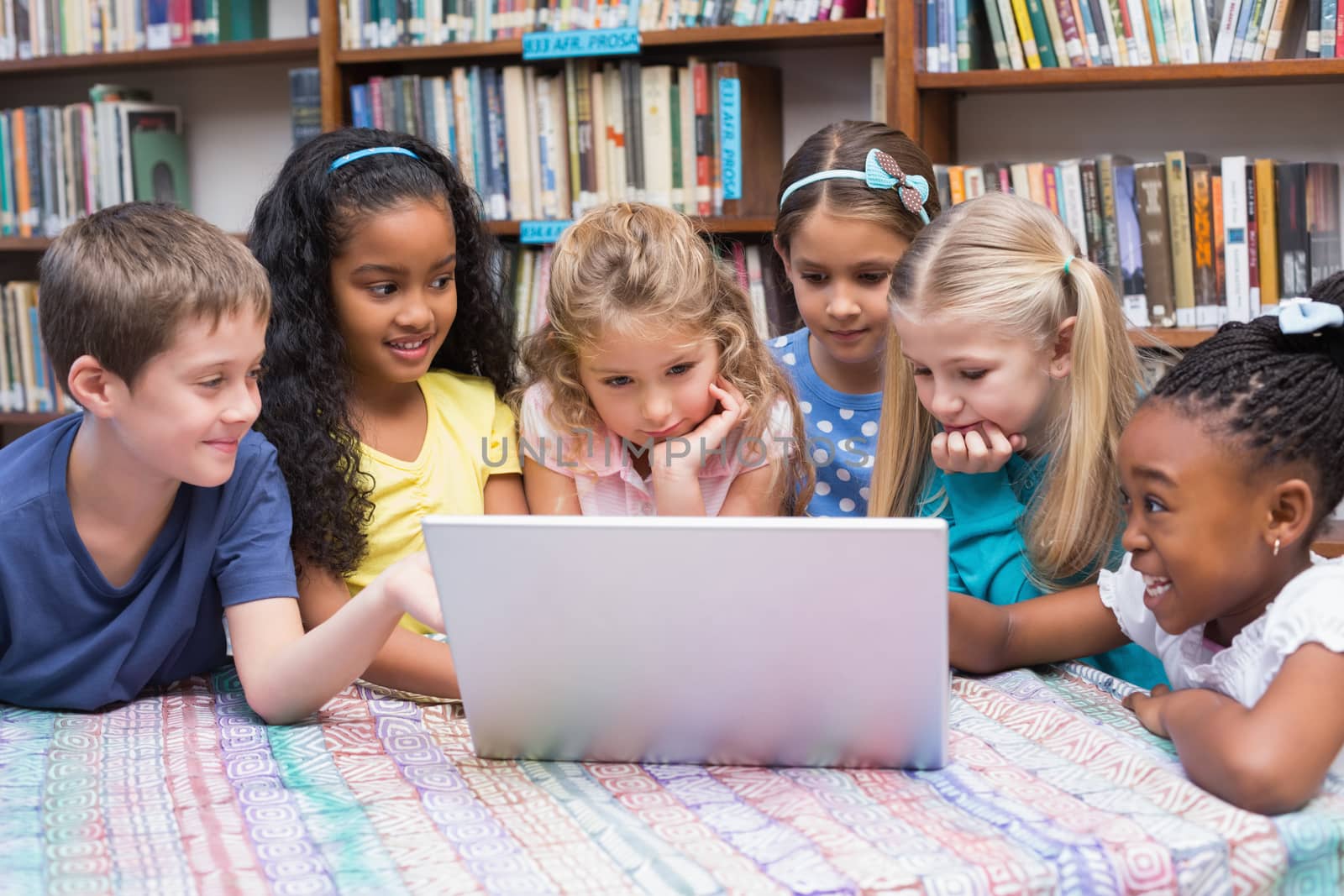 Cute pupils looking at laptop in library by Wavebreakmedia