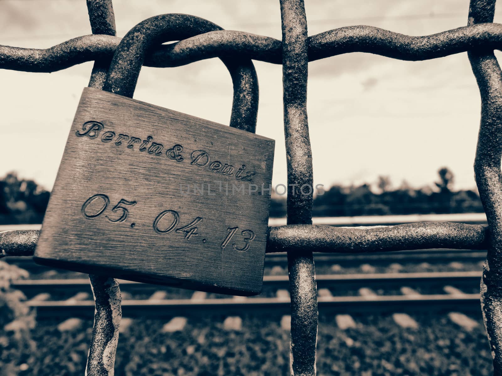 Monochrome close up of an old rusty padlock chained to a railing.
