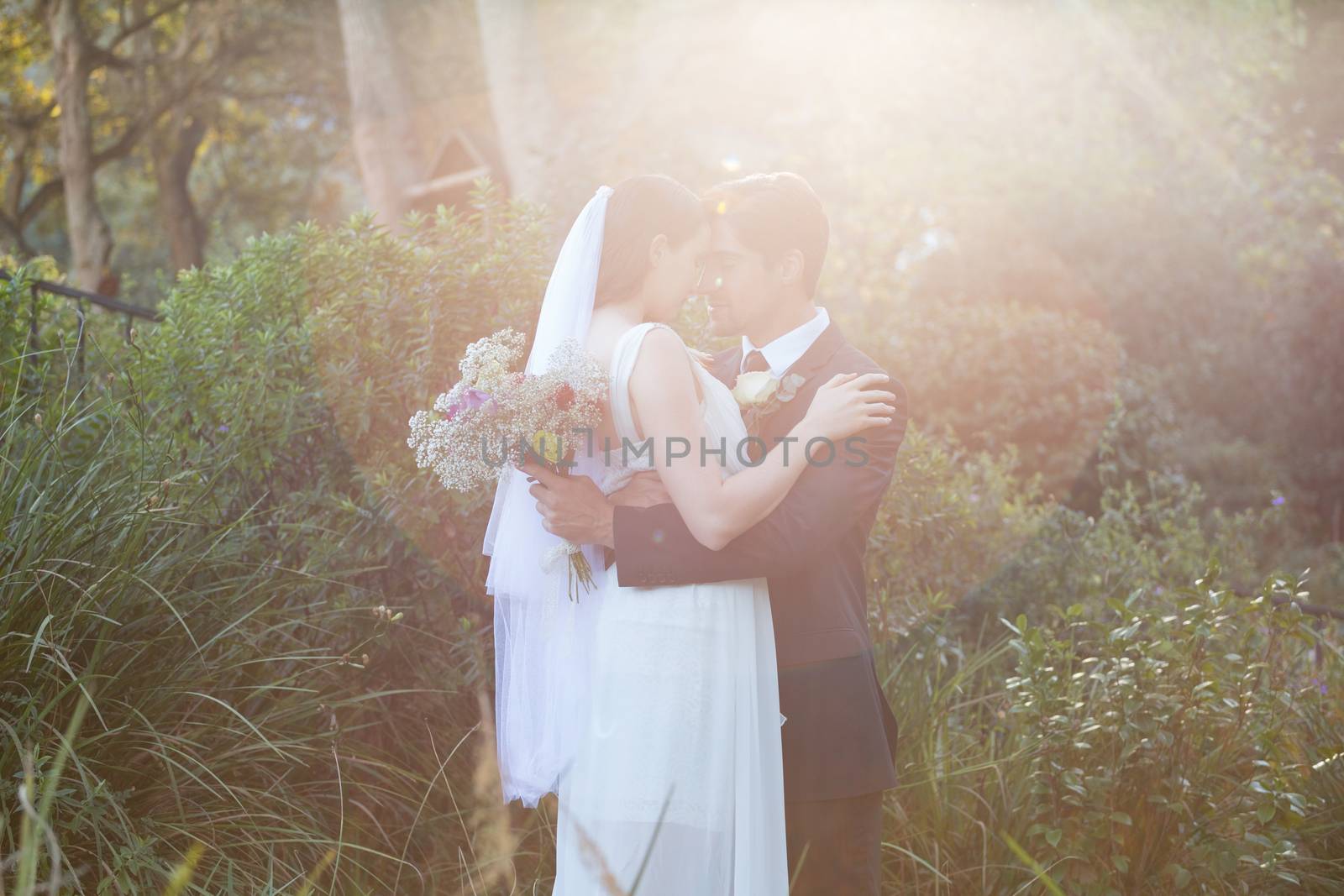 Romantic newlywed couple with eyes closed embracing while standing in park