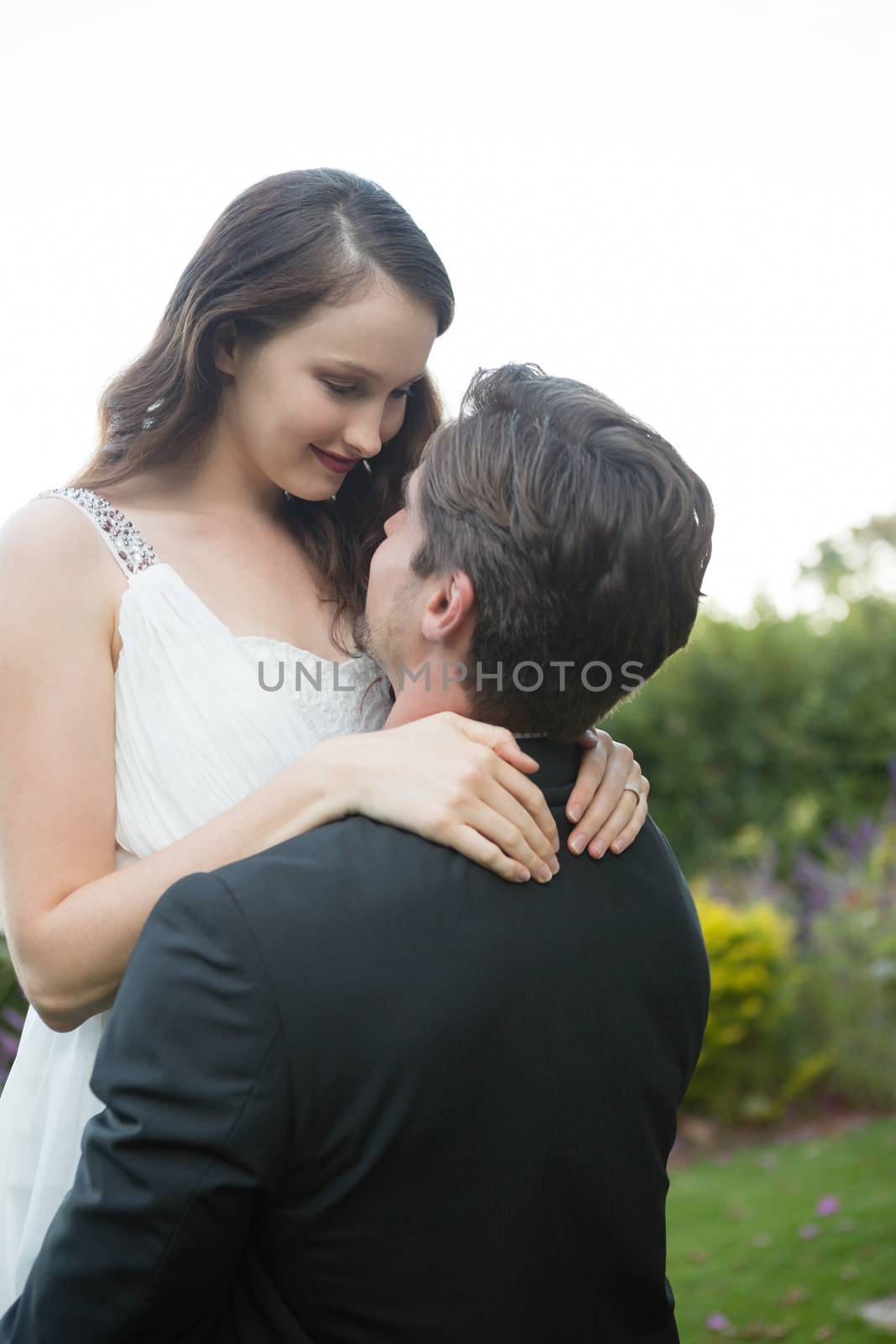 Romantic bridegroom lifting bride while standing against clear sky in park