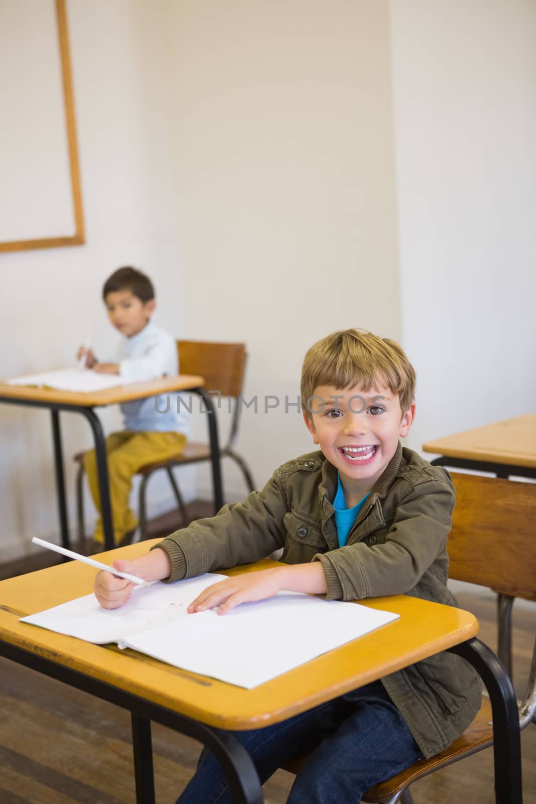 Pupil writing in notepad at his desk smiling at camera by Wavebreakmedia