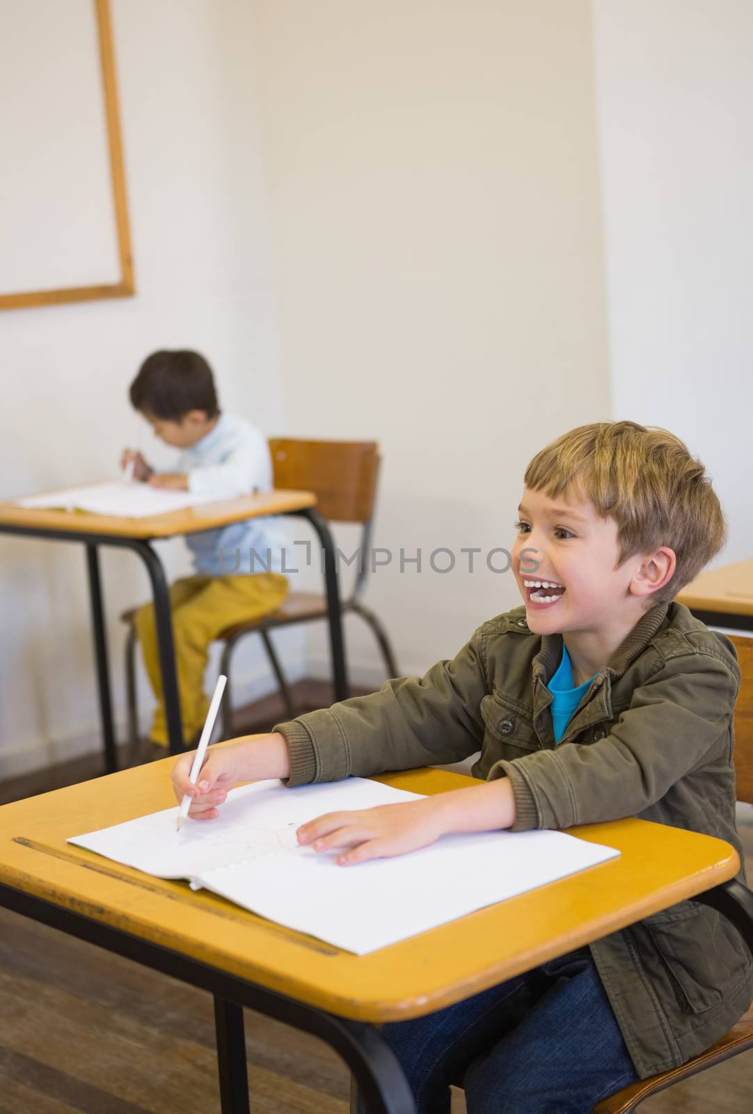 Pupil writing in notepad at his desk smiling at the elementary school