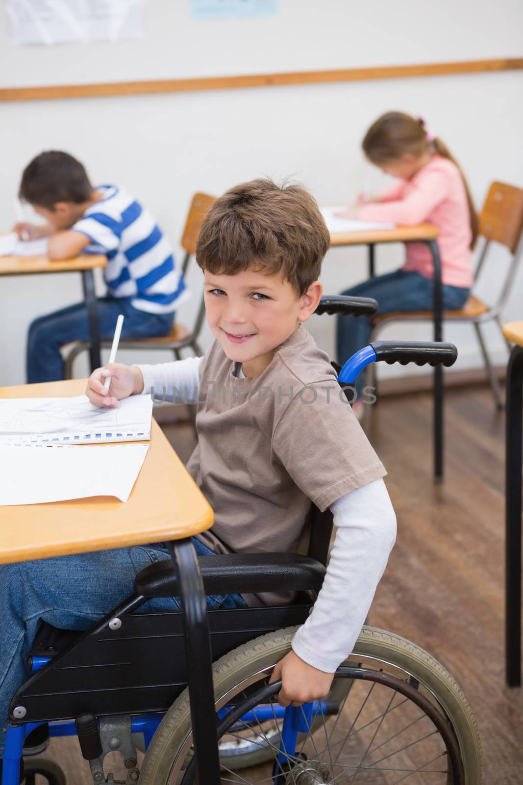 Disabled pupil writing at desk in classroom by Wavebreakmedia