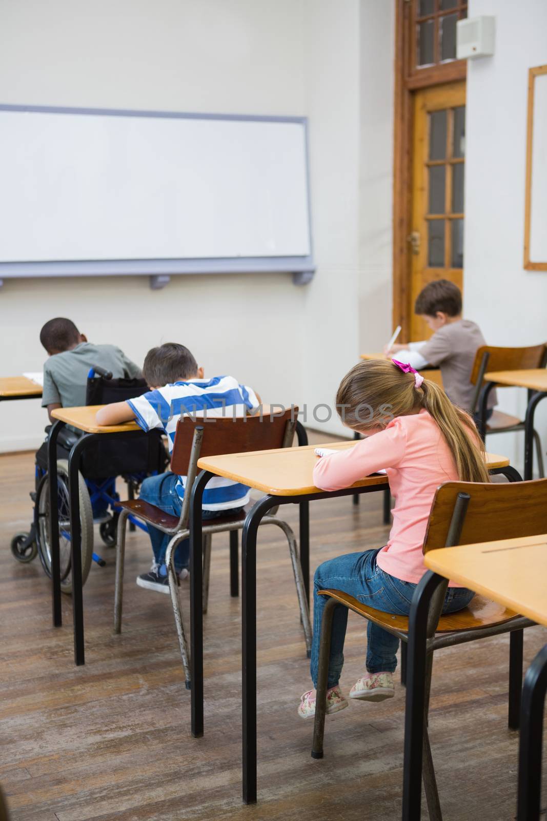 Cute pupils writing at desks in classroom by Wavebreakmedia