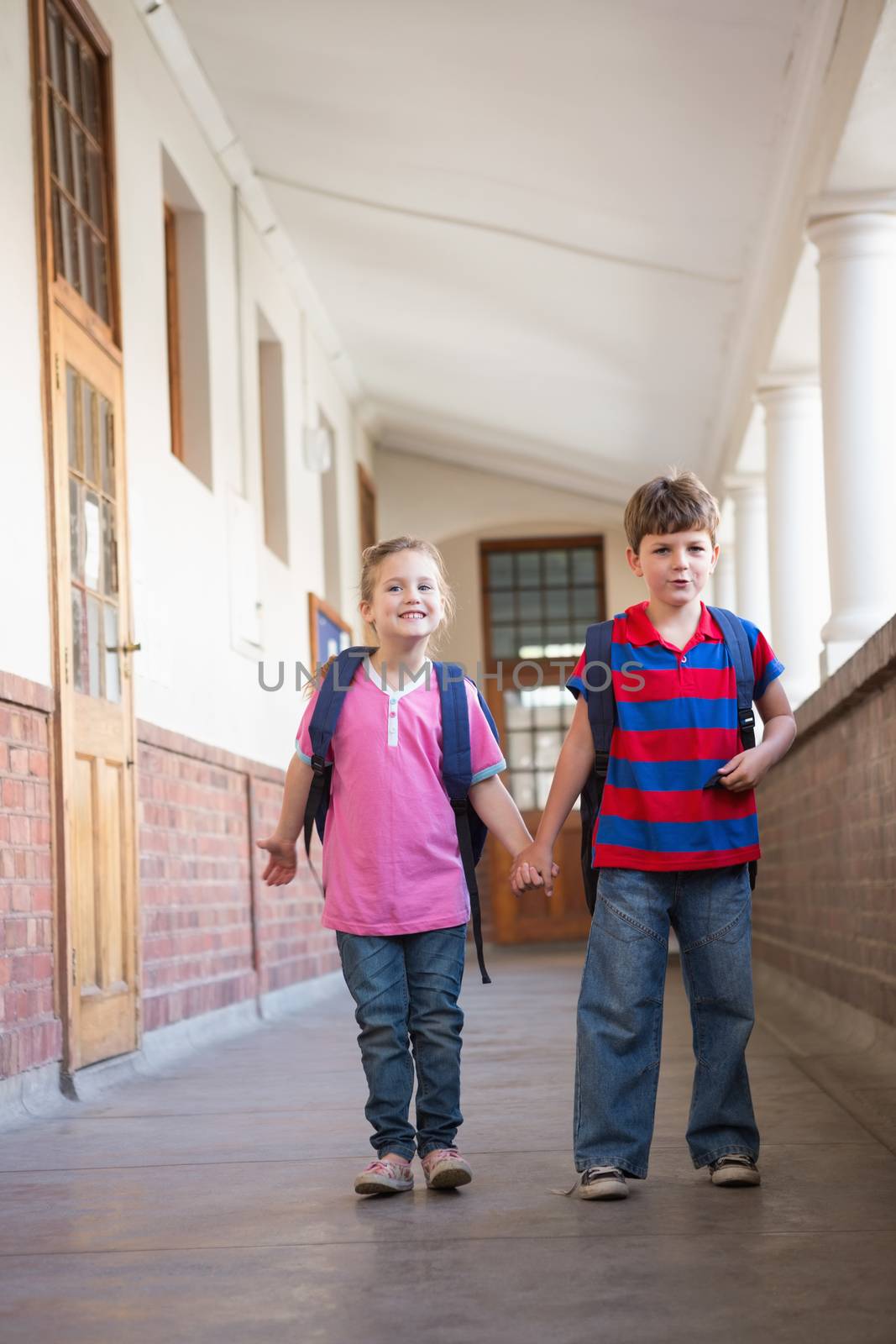 Cute pupils holding hands in corridor at the elementary school