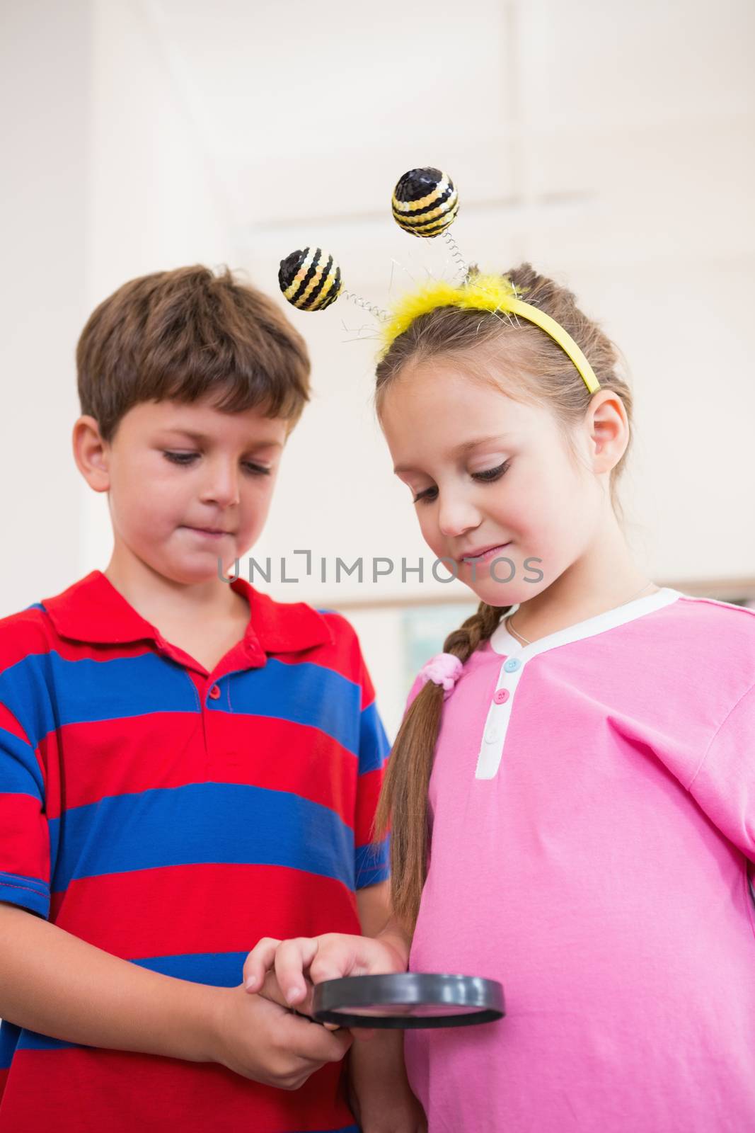 Cute pupils looking through magnifying glass at the elementary school