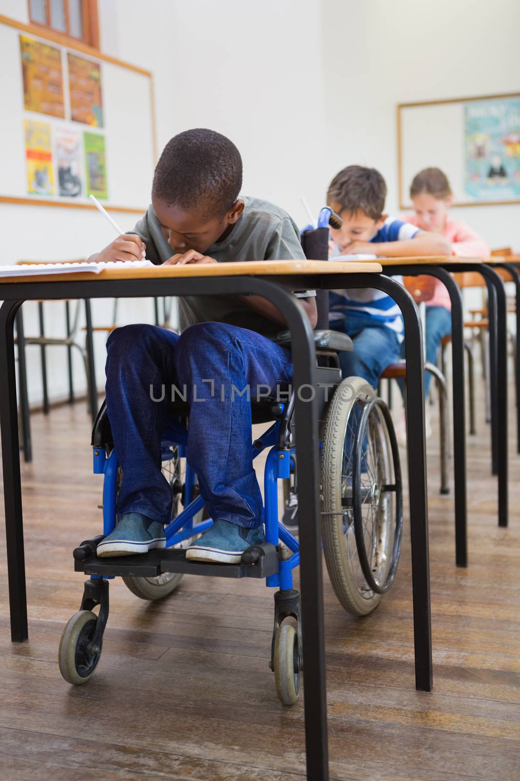 Disabled pupil writing at desk in classroom by Wavebreakmedia