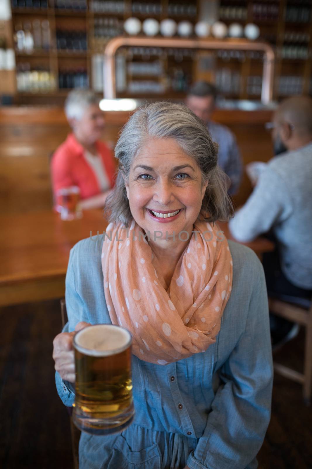 Portrait of smiling senior woman holding glass of beer in bar
