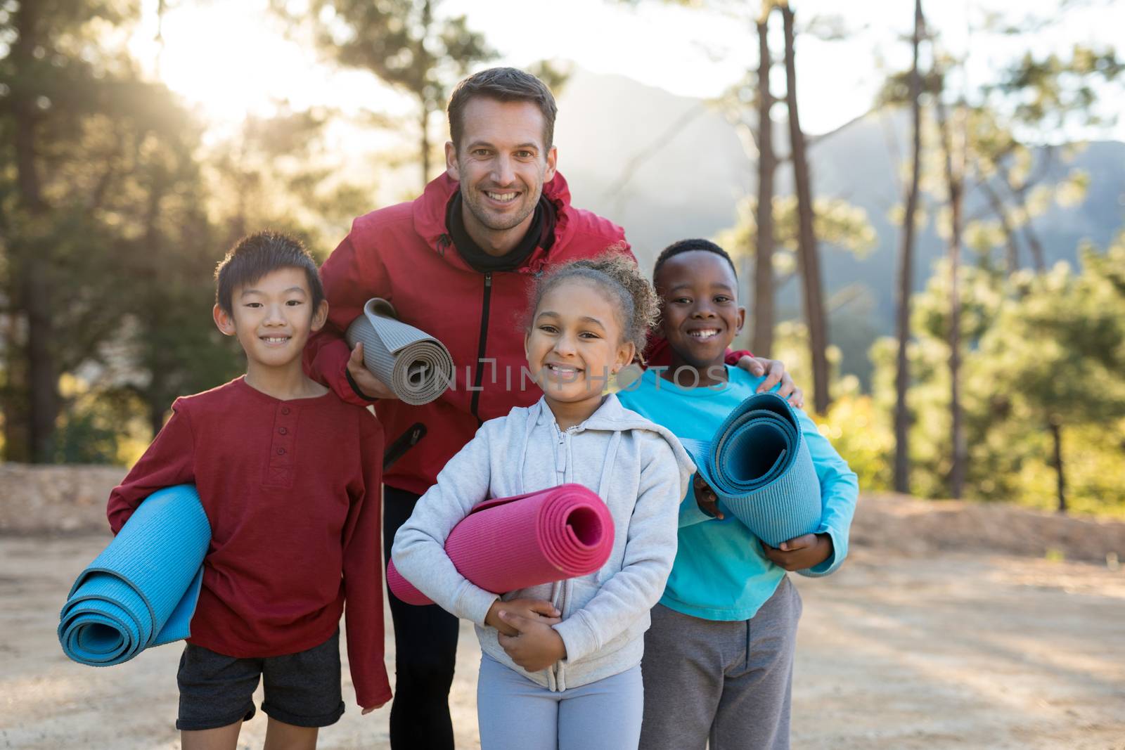 Portrait of coach and kids standing with yoga mat in park
