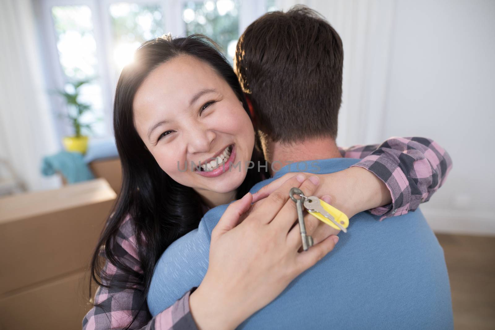 Couple embracing each other while holding keys of new home by Wavebreakmedia