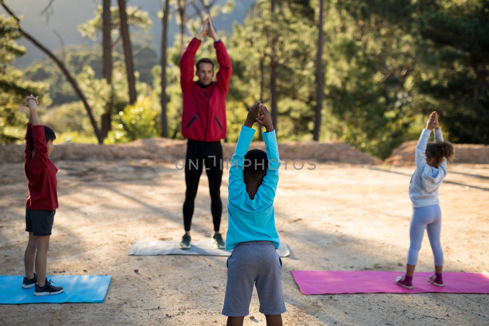 Coach assisting kids in practicing yoga on a sunny day