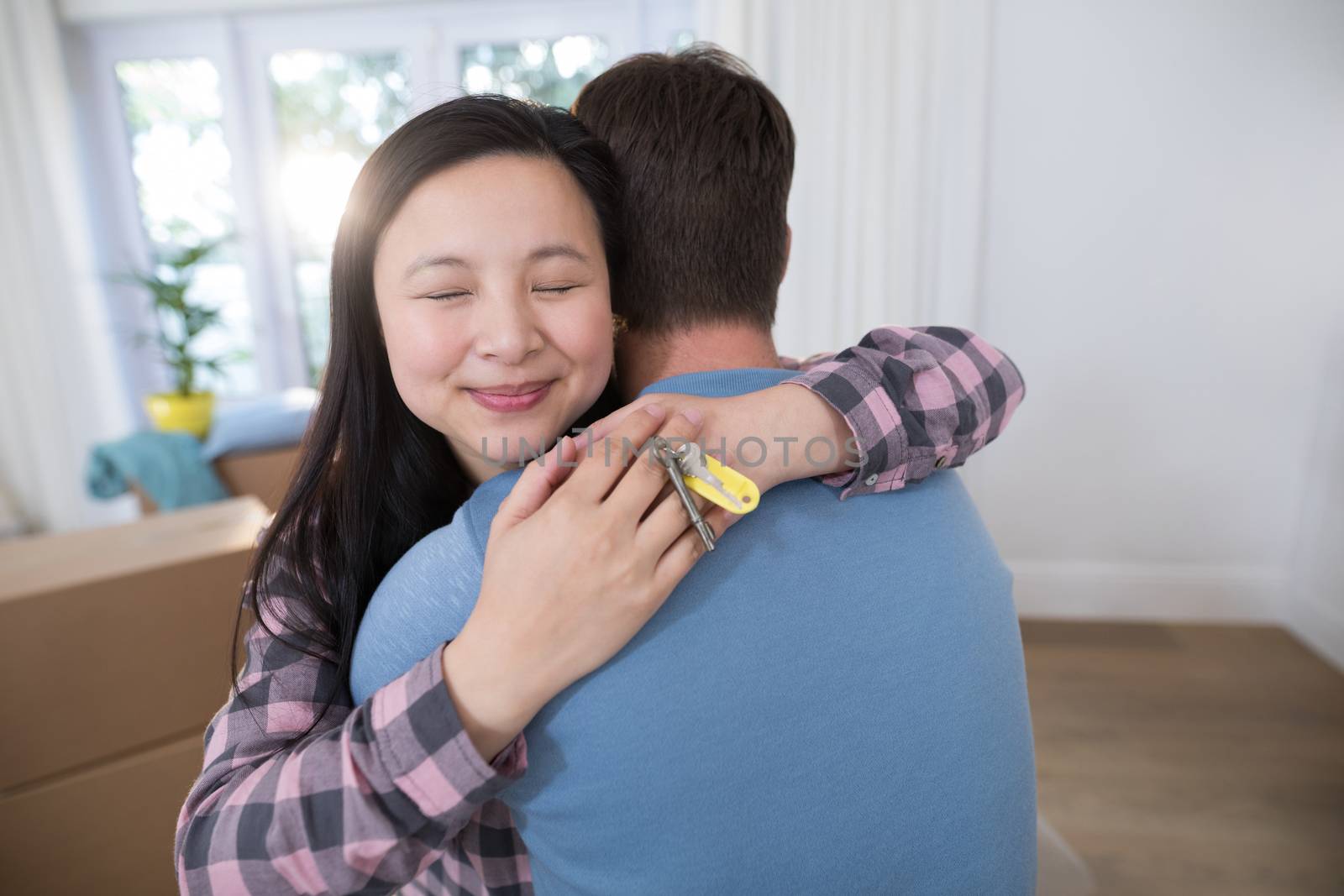 Couple embracing each other while holding keys of new home by Wavebreakmedia