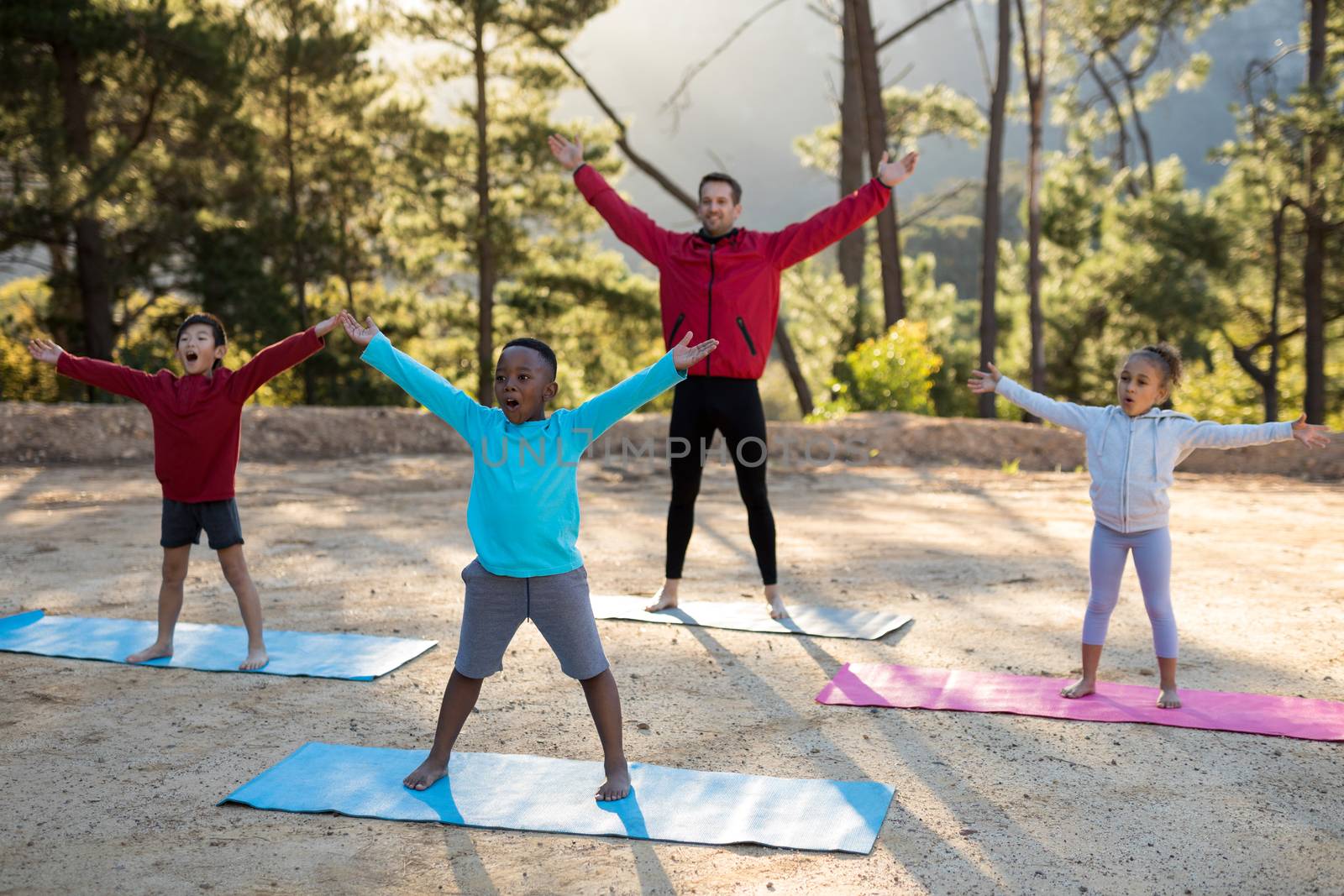 Coach assisting kids in practicing yoga on a sunny day