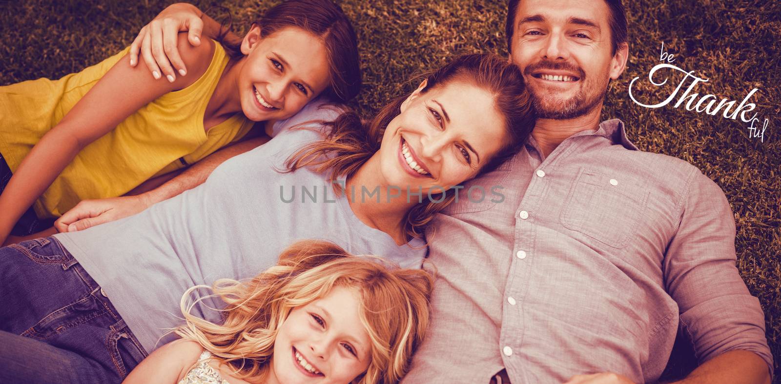 Digital image of happy thanksgiving day text greeting against portrait of happy family lying on field