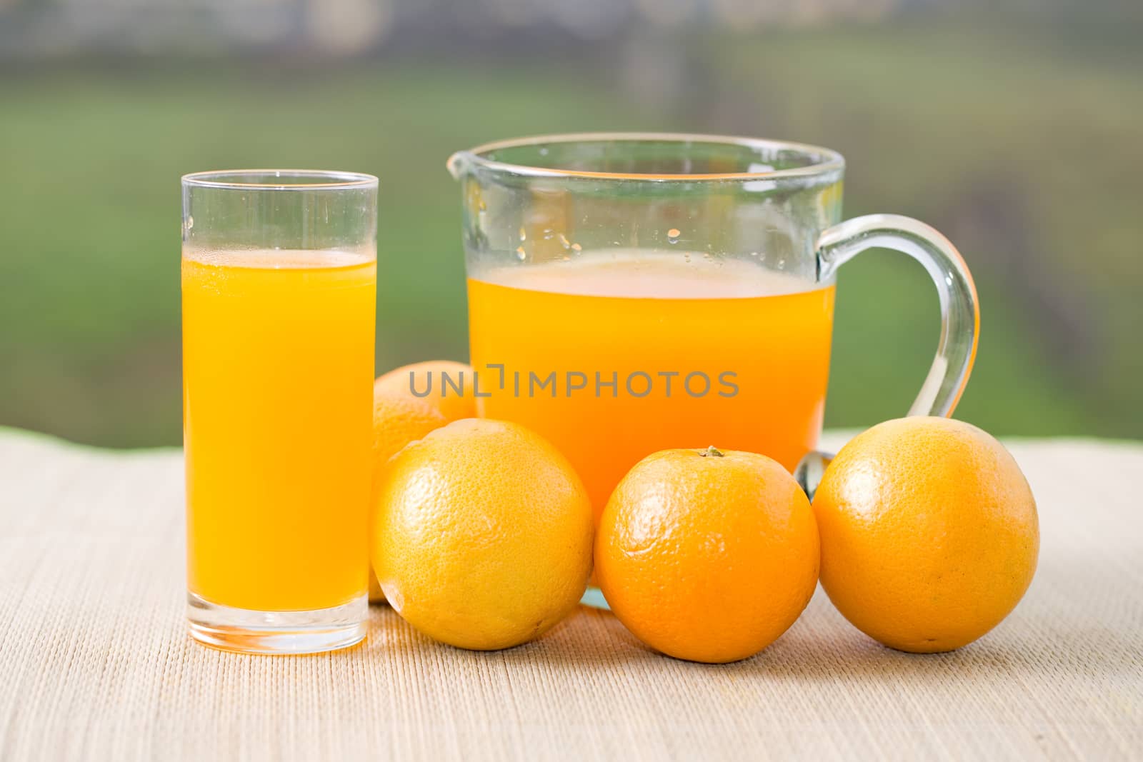 glass of delicious orange juice and oranges on table in garden