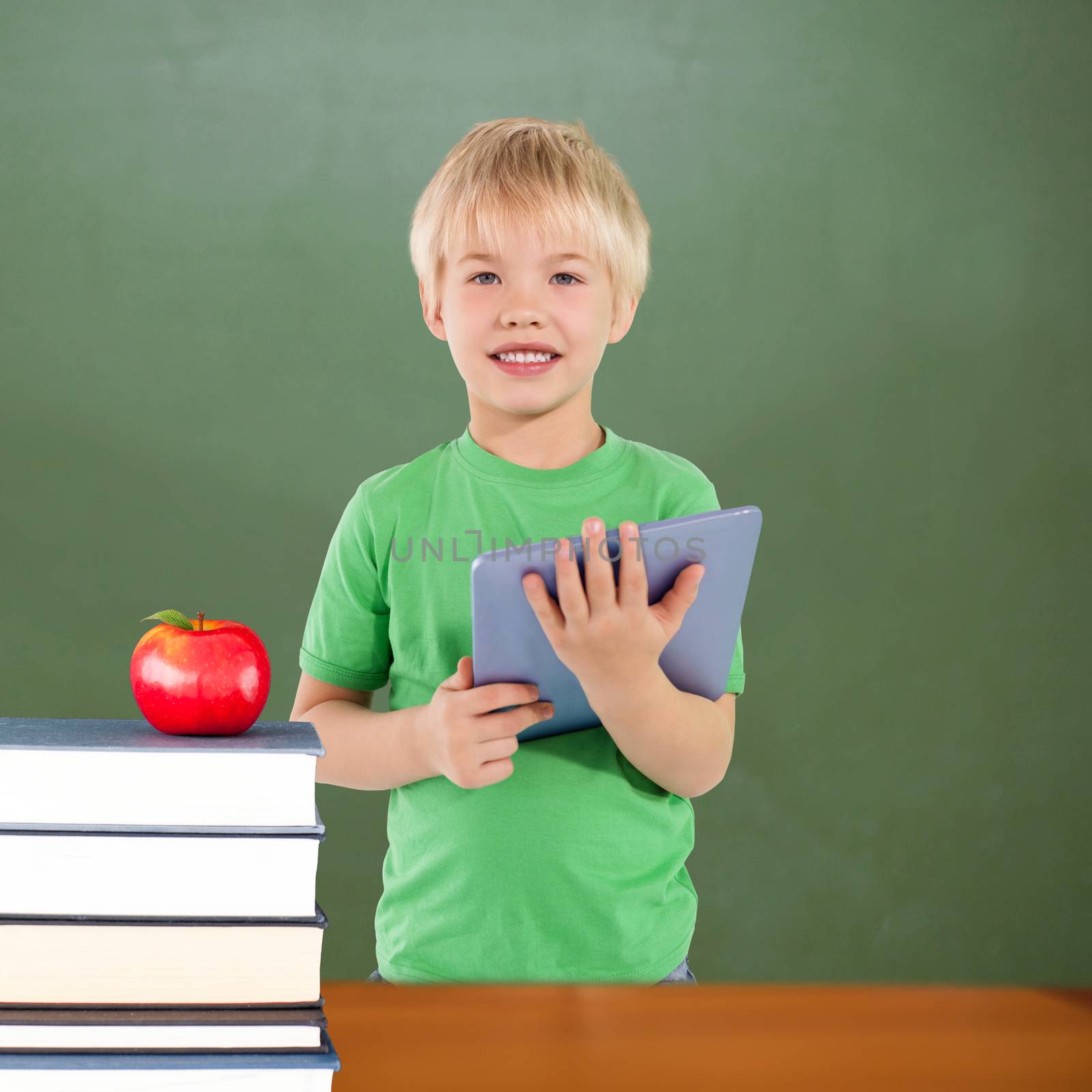Cute boy using tablet against red apple on pile of books in classroom