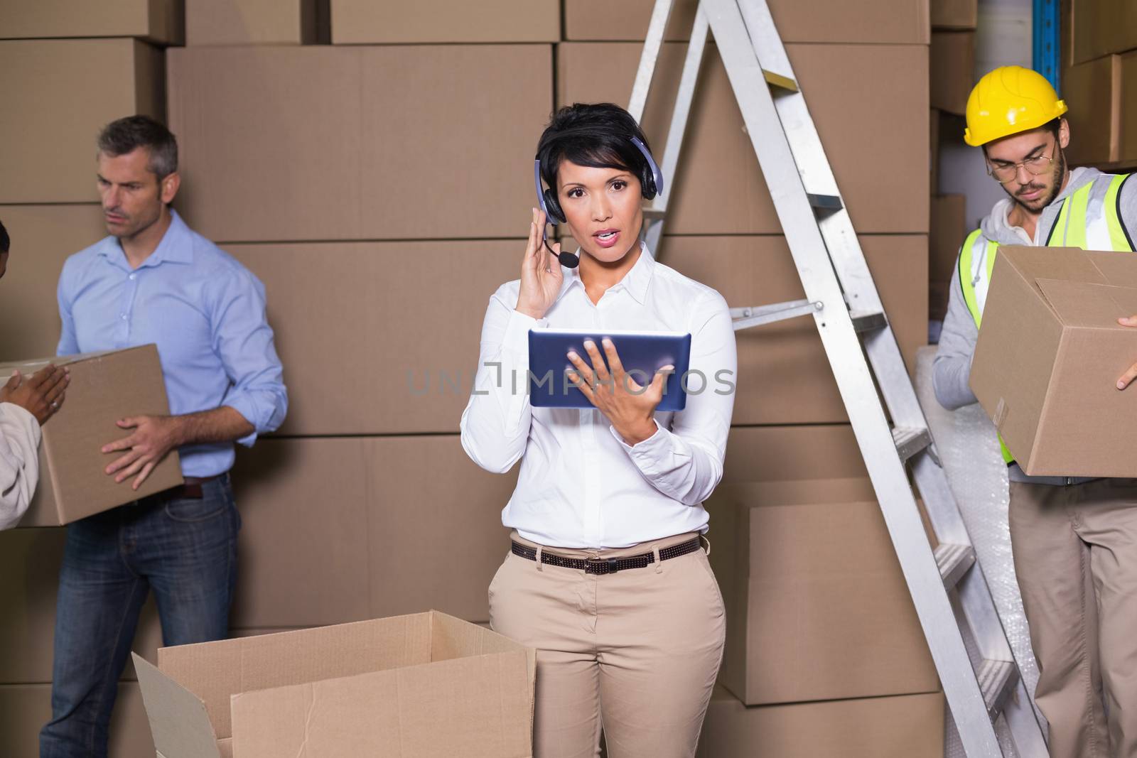 Pretty warehouse manager using tablet during busy period in a large warehouse