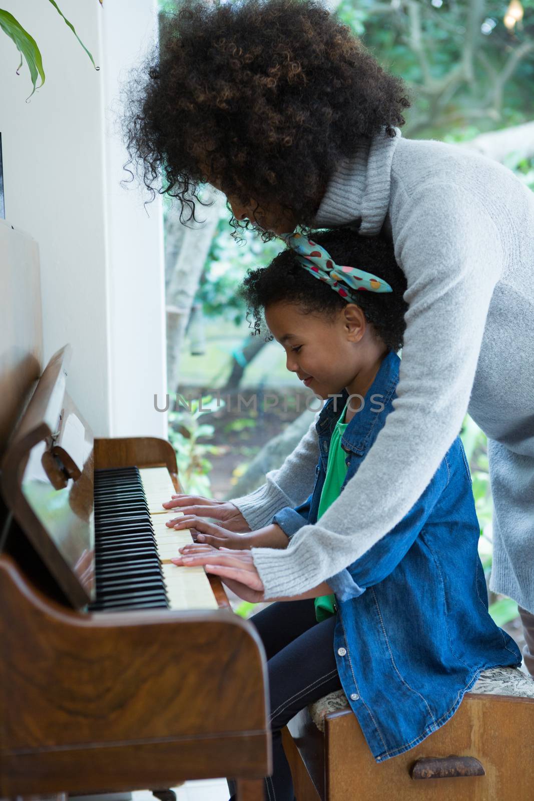 Mother assisting daughter in playing piano at home