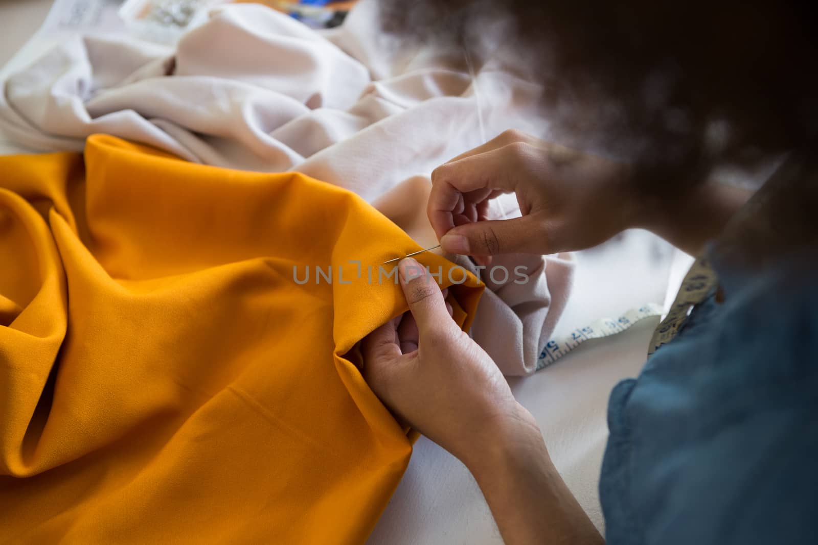 Female fashion designer stitching cloth with needle at table