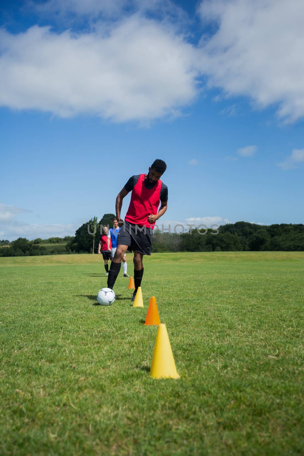 Soccer player dribbling through cones in the ground on a sunny day