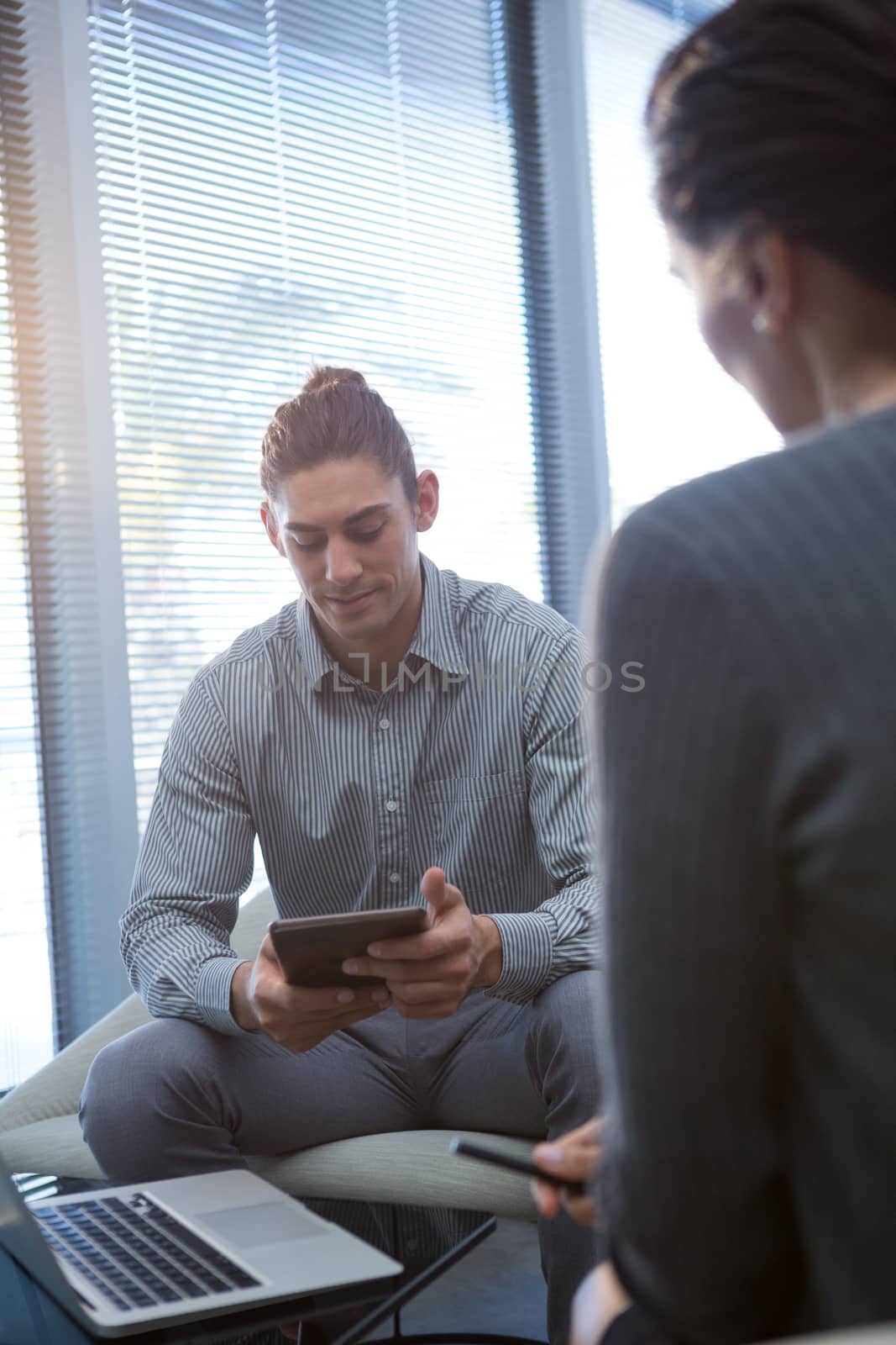 Colleagues using digital tablet in waiting area of office