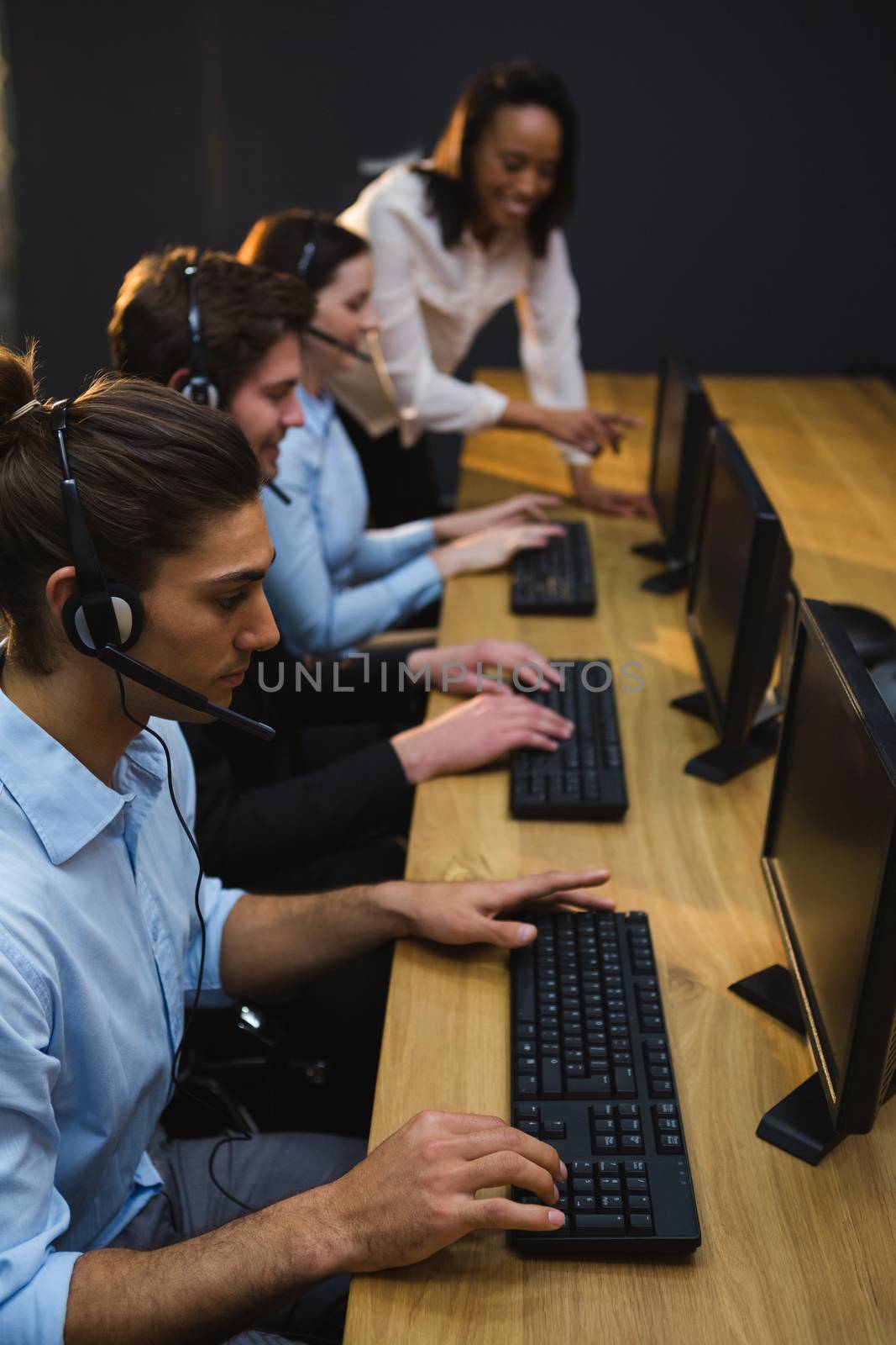 Business executives with headsets using computers at desk in office