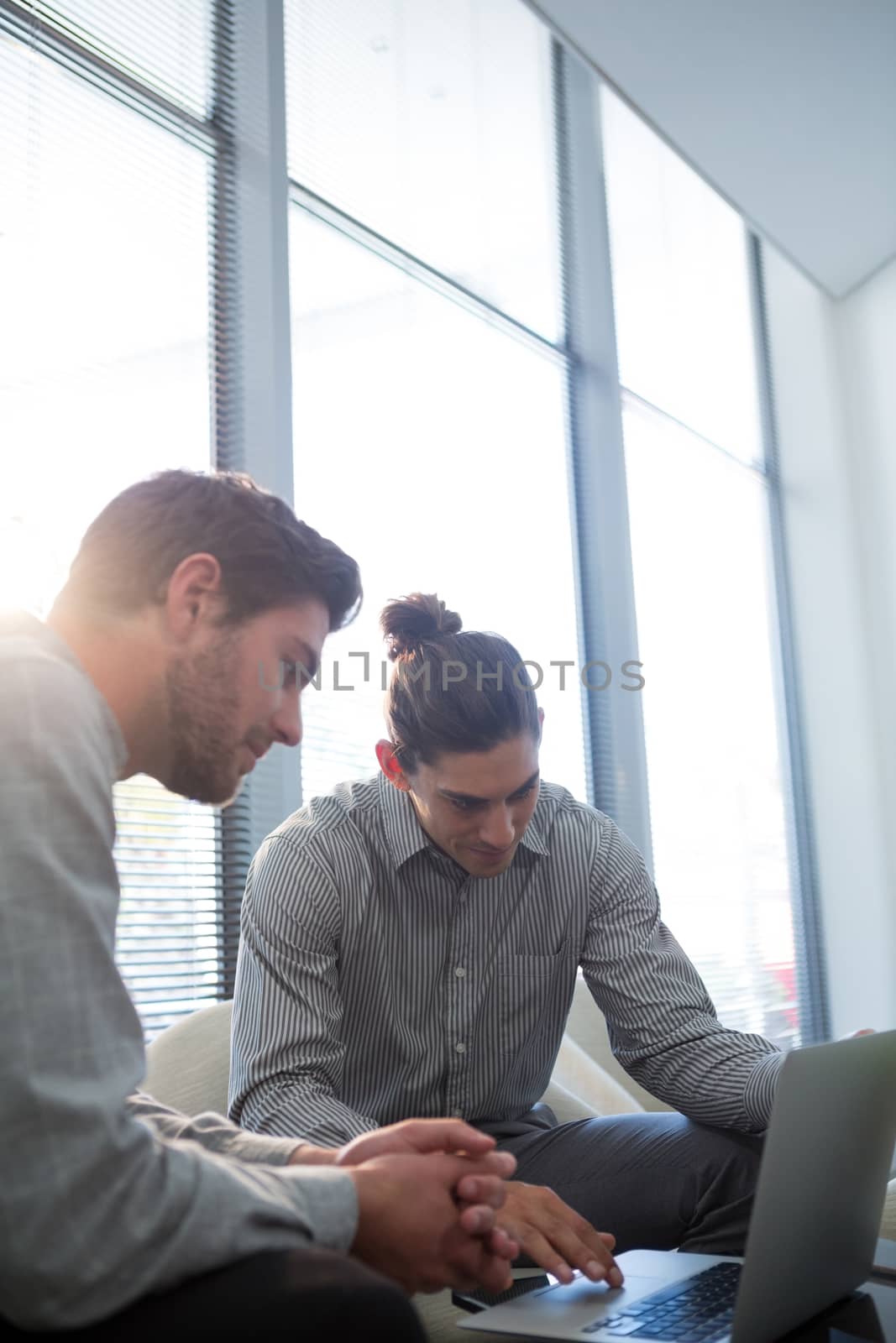 Colleagues discussing over laptop in waiting area of office