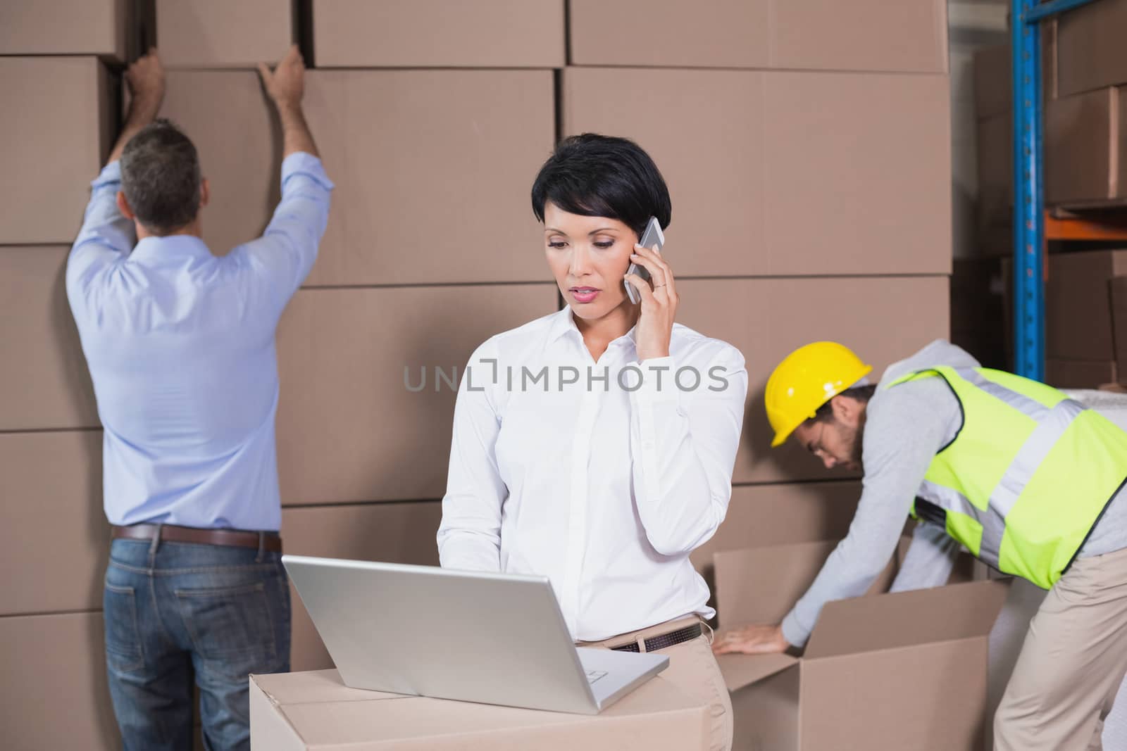 Warehouse manager using laptop and talking on phone by Wavebreakmedia