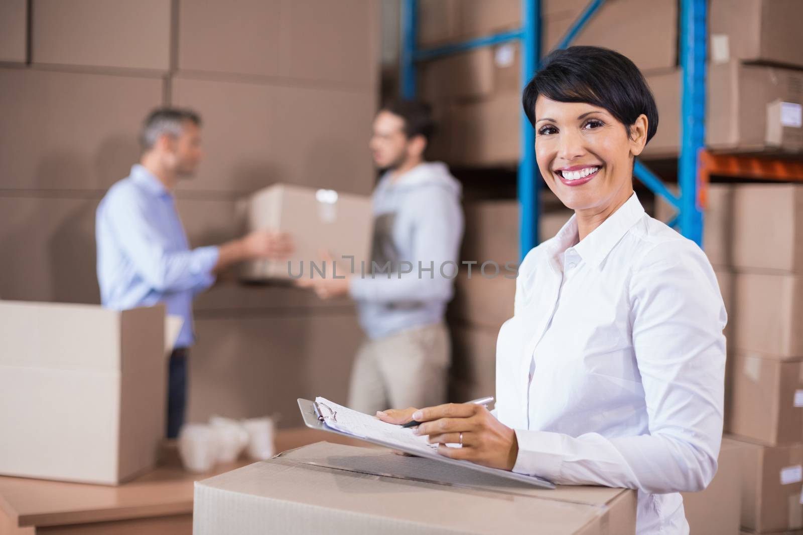 Warehouse manager writing on clipboard in a large warehouse