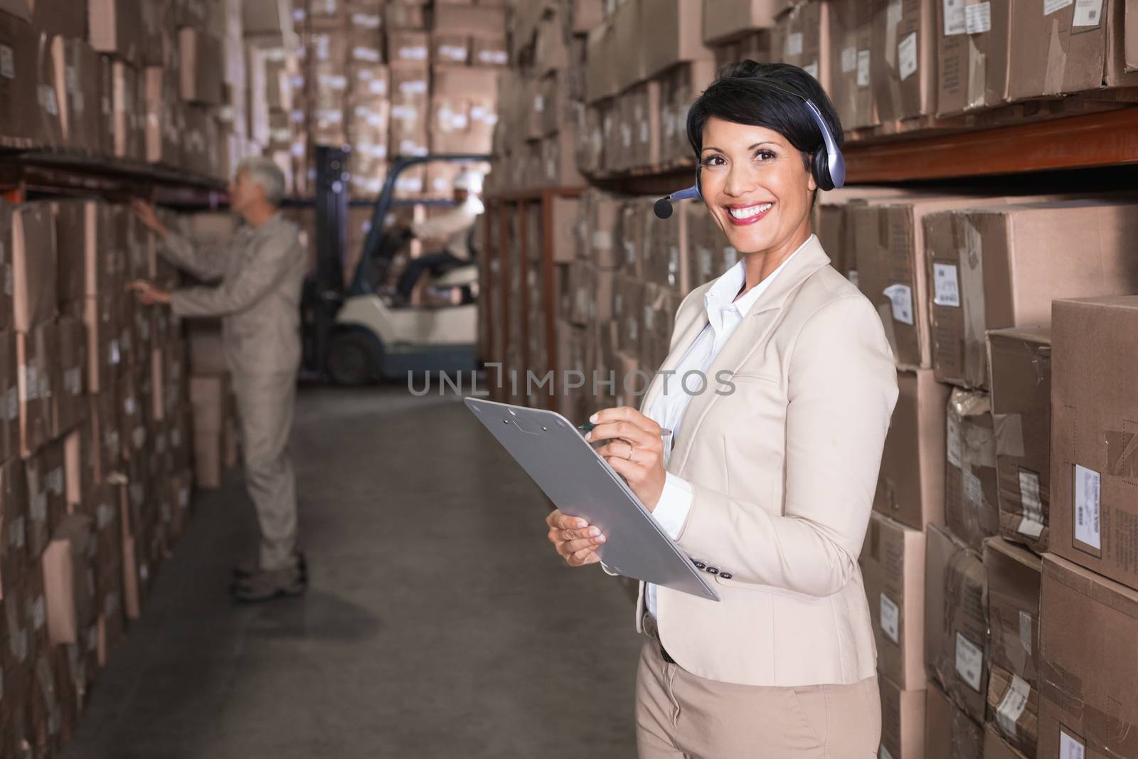 Pretty warehouse manager writing on clipboard in a large warehouse