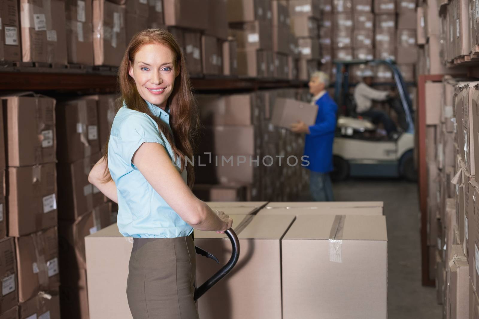 Warehouse manager smiling at camera with trolley in a large warehouse