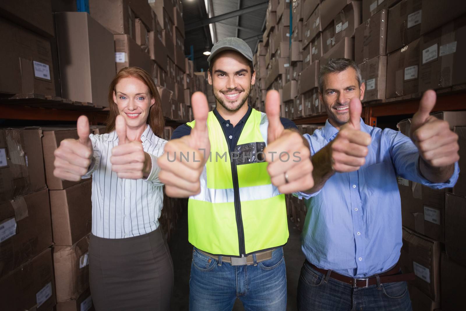 Warehouse team smiling at camera showing thumbs up in a large warehouse