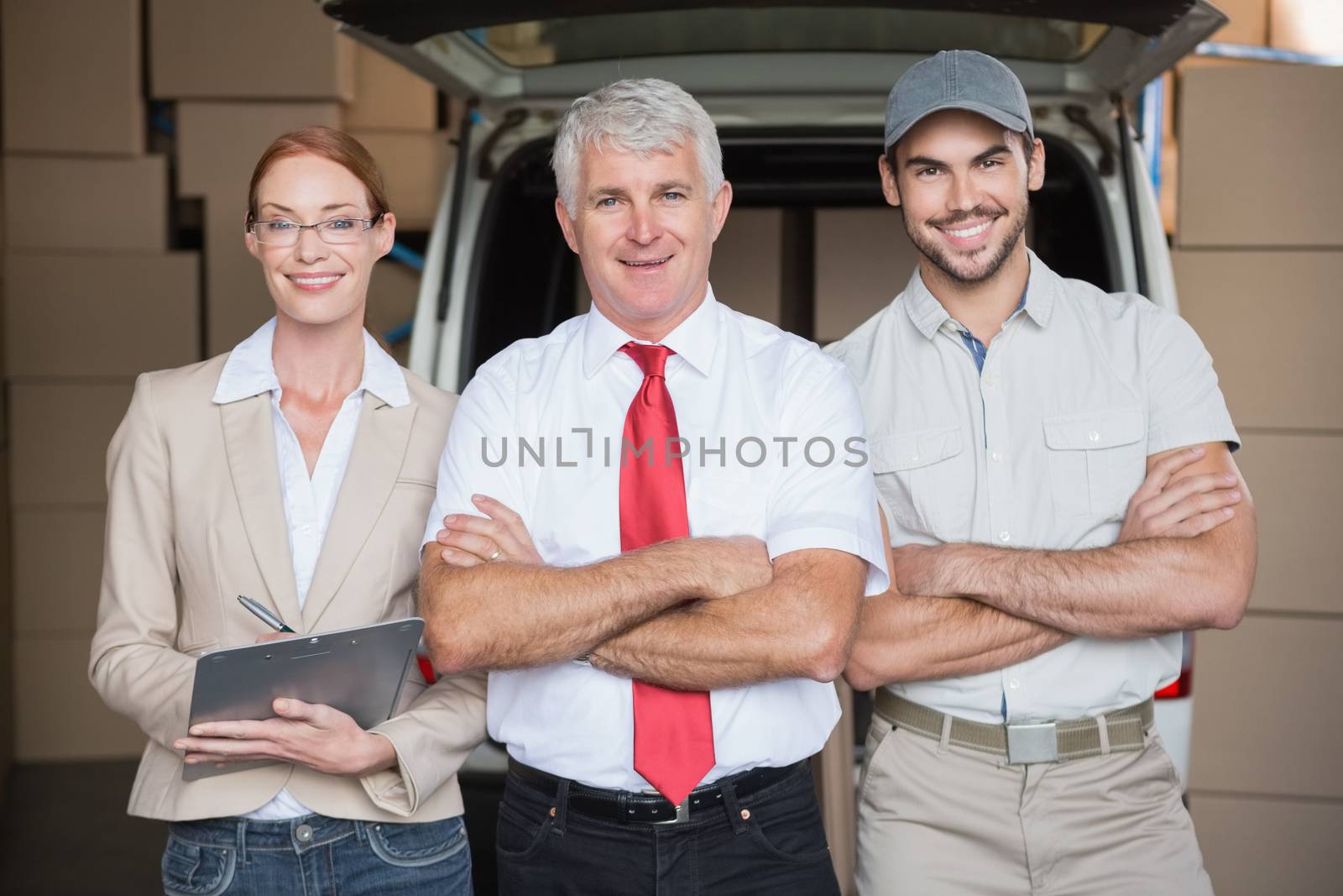 Warehouse managers and delivery driver smiling at camera in a large warehouse