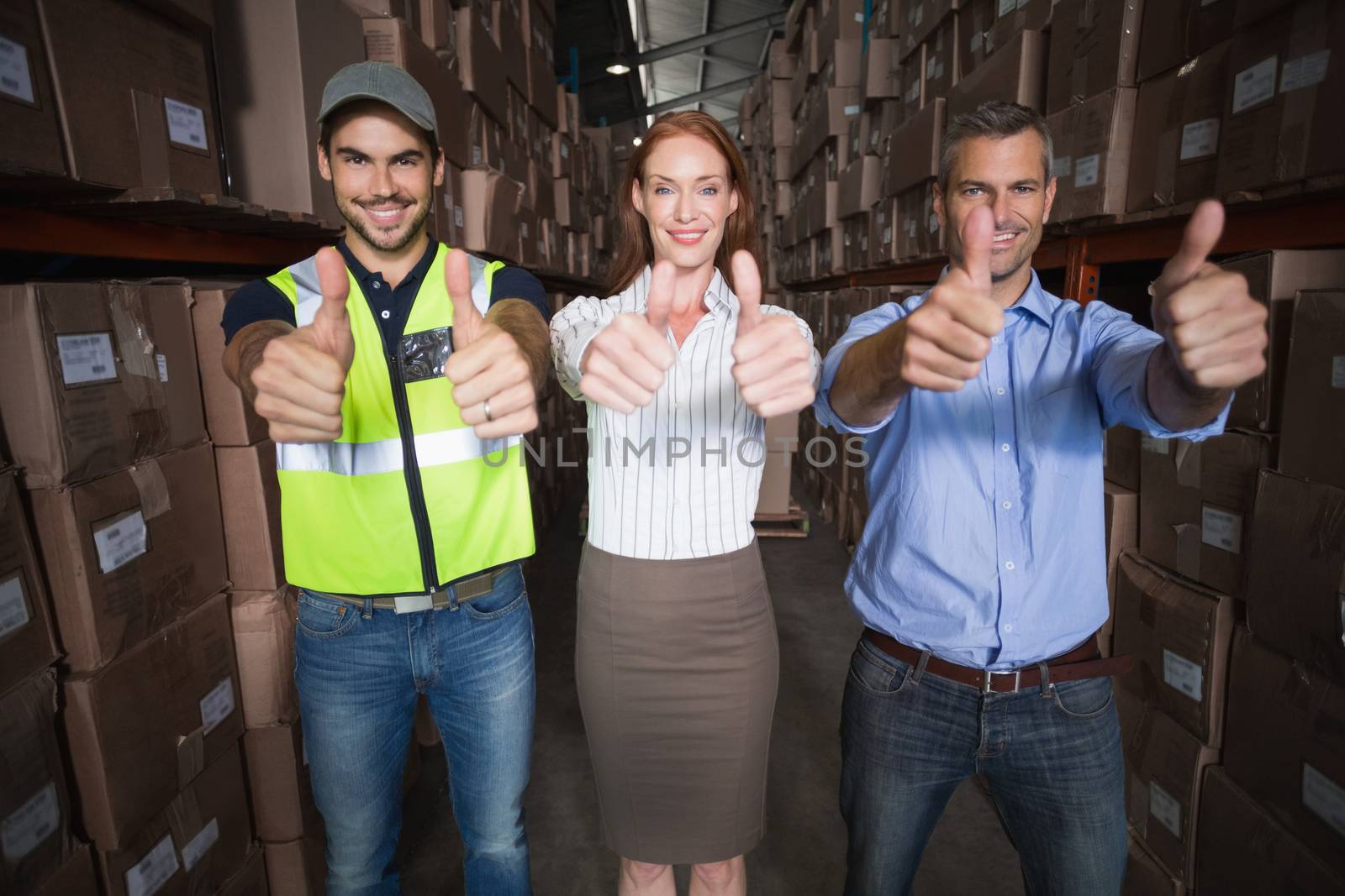 Warehouse team smiling at camera showing thumbs up in a large warehouse